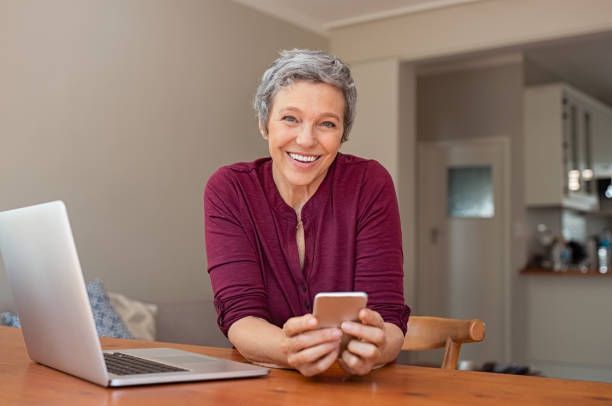 A woman is sitting at a table with a laptop and a cell phone.