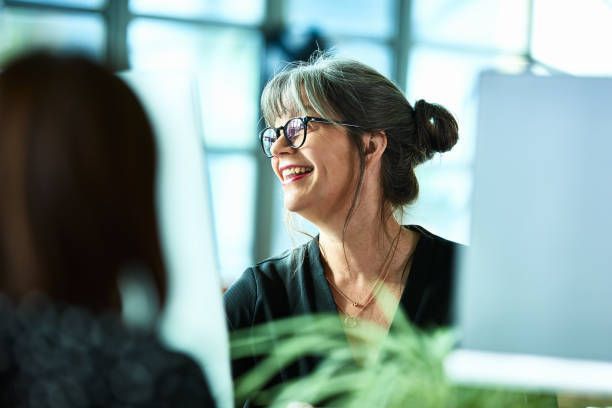 A woman wearing glasses is smiling while sitting in front of a computer.