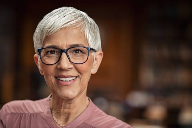 An older woman wearing glasses and a pink shirt is smiling for the camera.