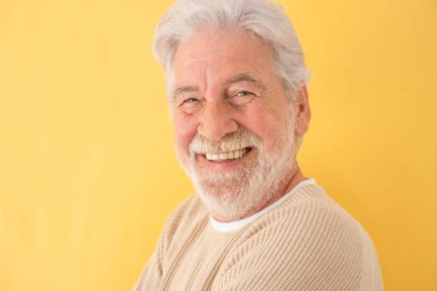 An elderly man with a beard is smiling and looking at the camera.