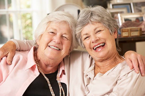 Two older women are sitting next to each other on a couch and smiling.