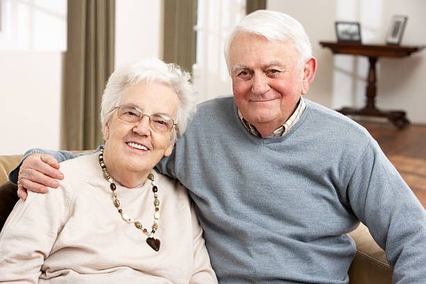 An elderly couple is posing for a picture while sitting on a couch.