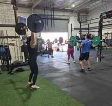 People in a gym performing overhead barbell lifts during a group fitness class.
