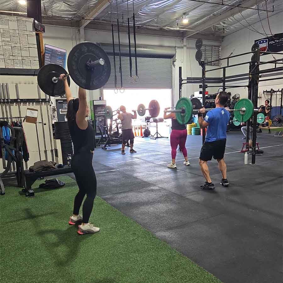 People in a gym performing overhead barbell lifts during a group fitness class.