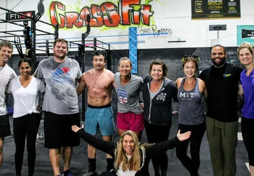 A group of eleven people standing and posing together in a CrossFit gym, one person crouching in the front center.