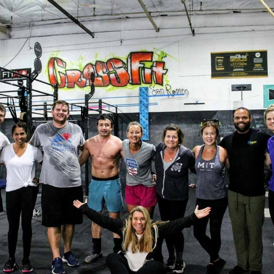 A group of people standing and smiling in a gym in front of a graffiti-style 