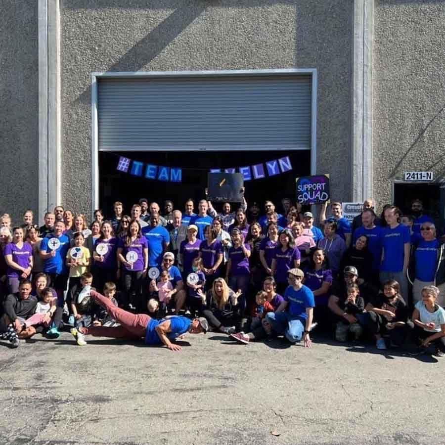 A large group wearing blue shirts poses in front of a warehouse with a 