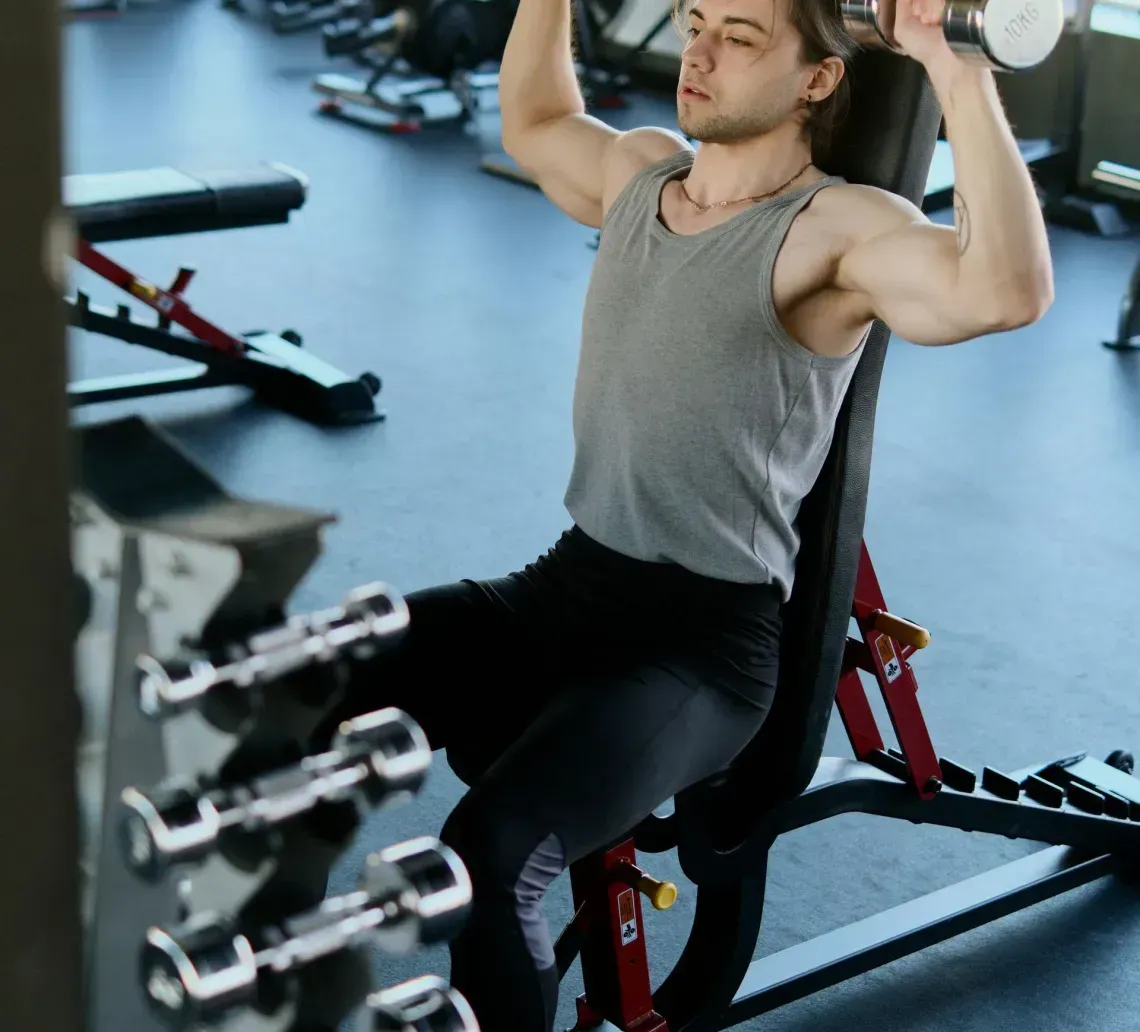 A person sitting on a gym bench performing a seated overhead dumbbell press.