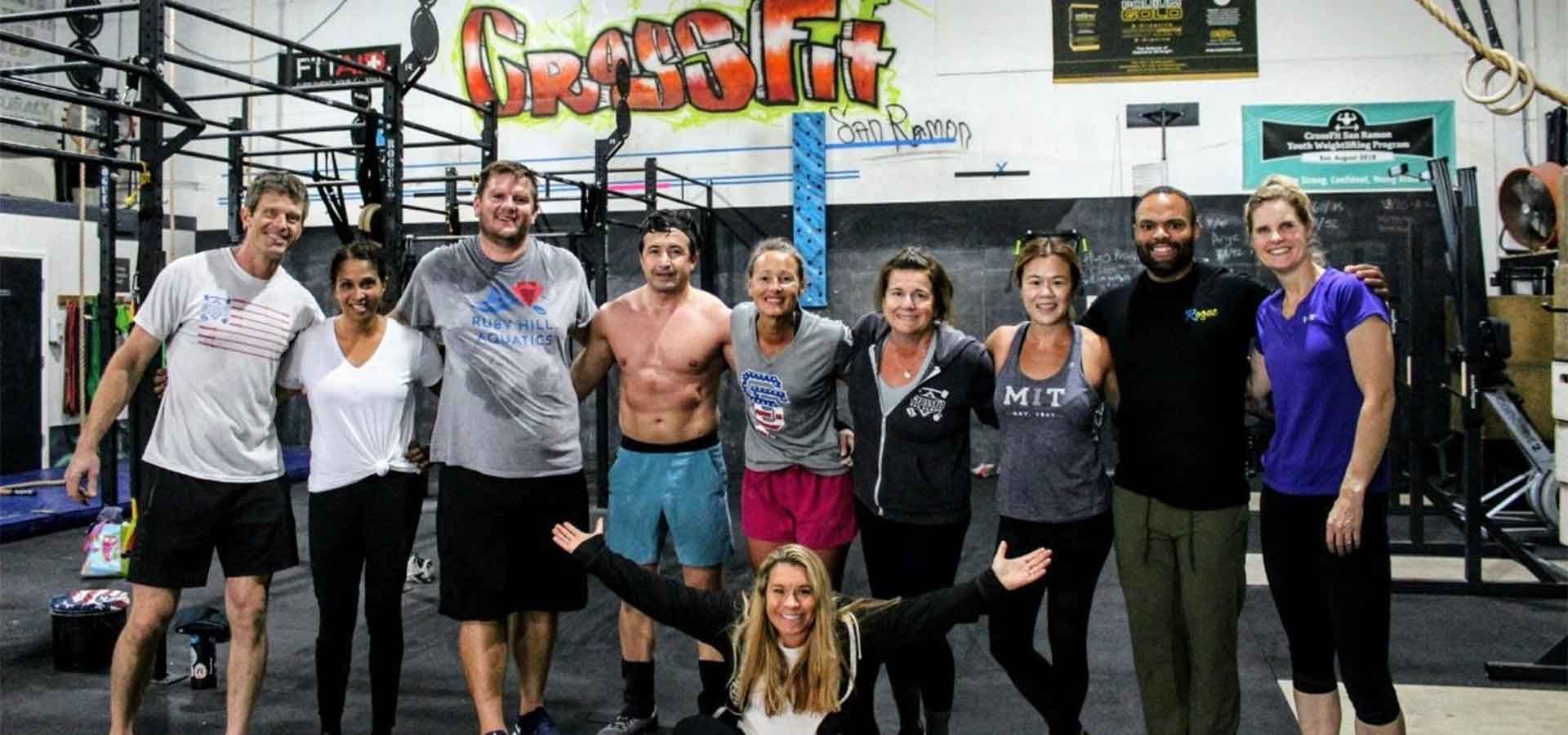 A group of eleven people standing and posing together in a CrossFit gym, one person crouching in the front center.