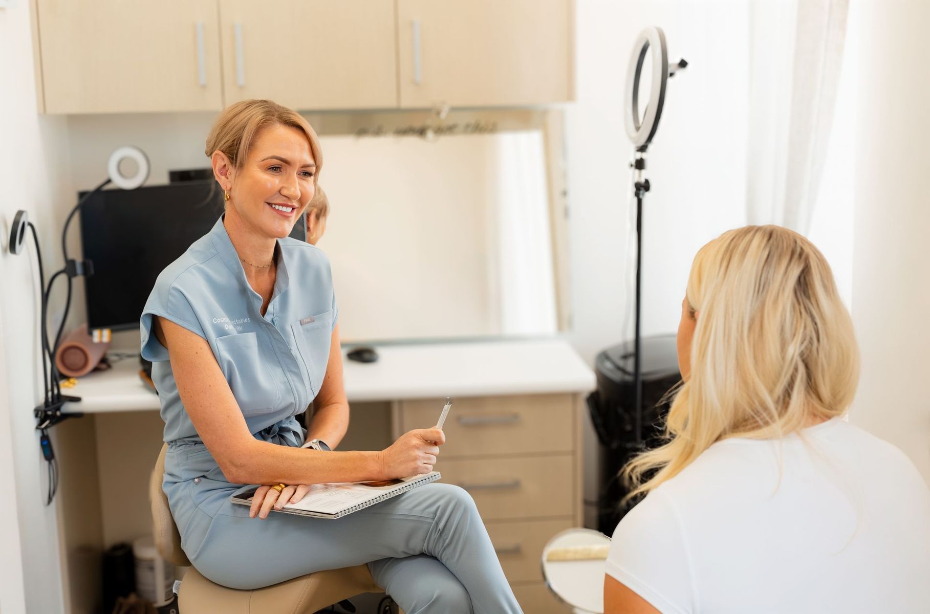 Woman in light blue top consults with patient in a clinic; both are smiling.