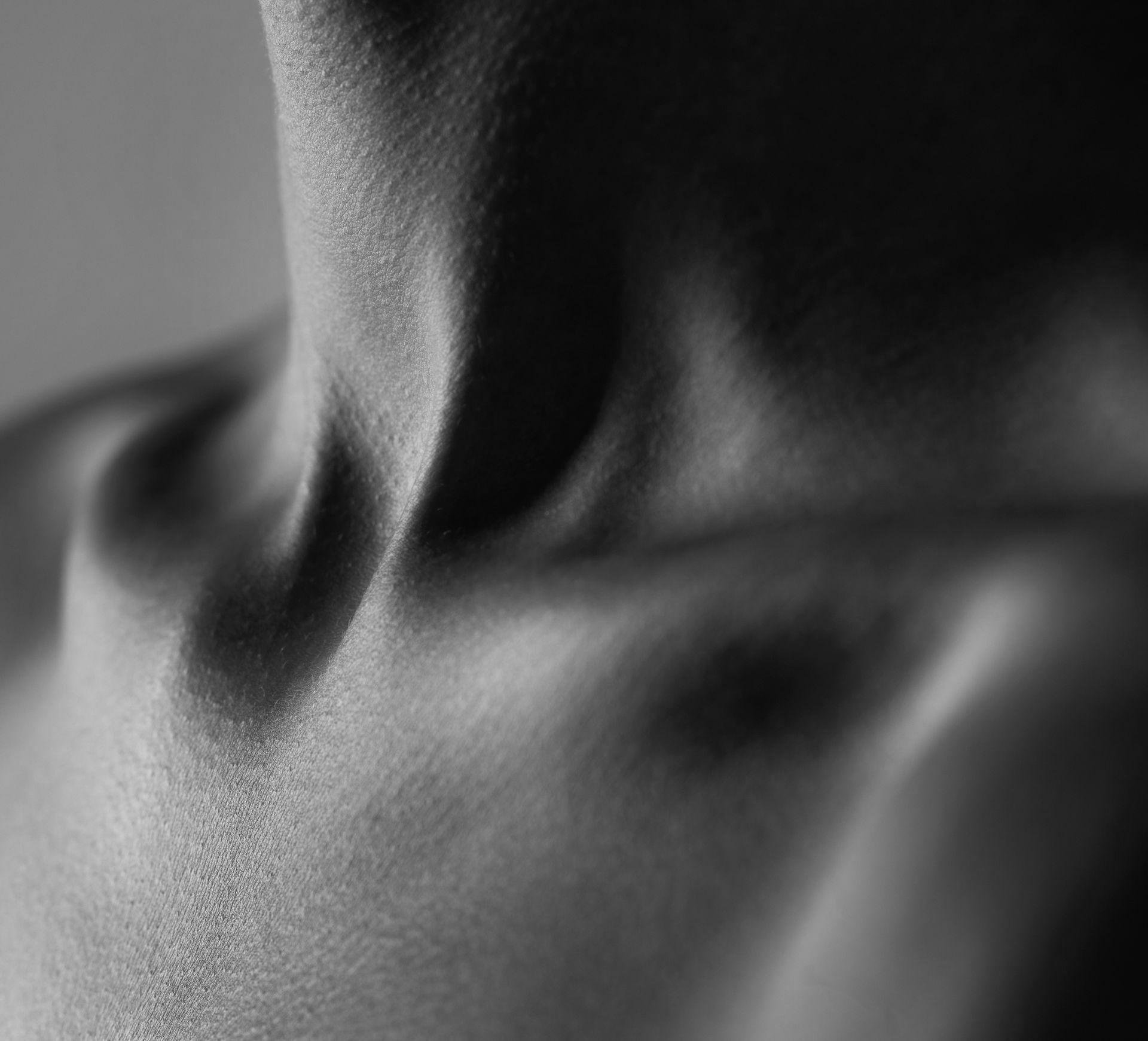 Black and white close-up of a person's collarbone, neck, and chest. Strong shadows highlight the anatomy.