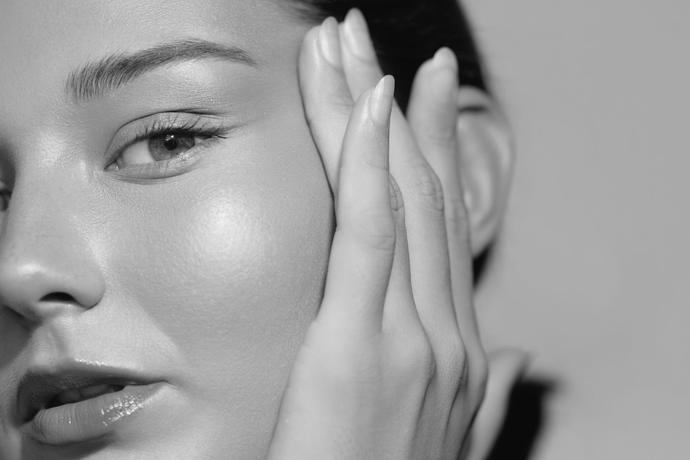 Black and white portrait of woman touching her face, with glowing skin.