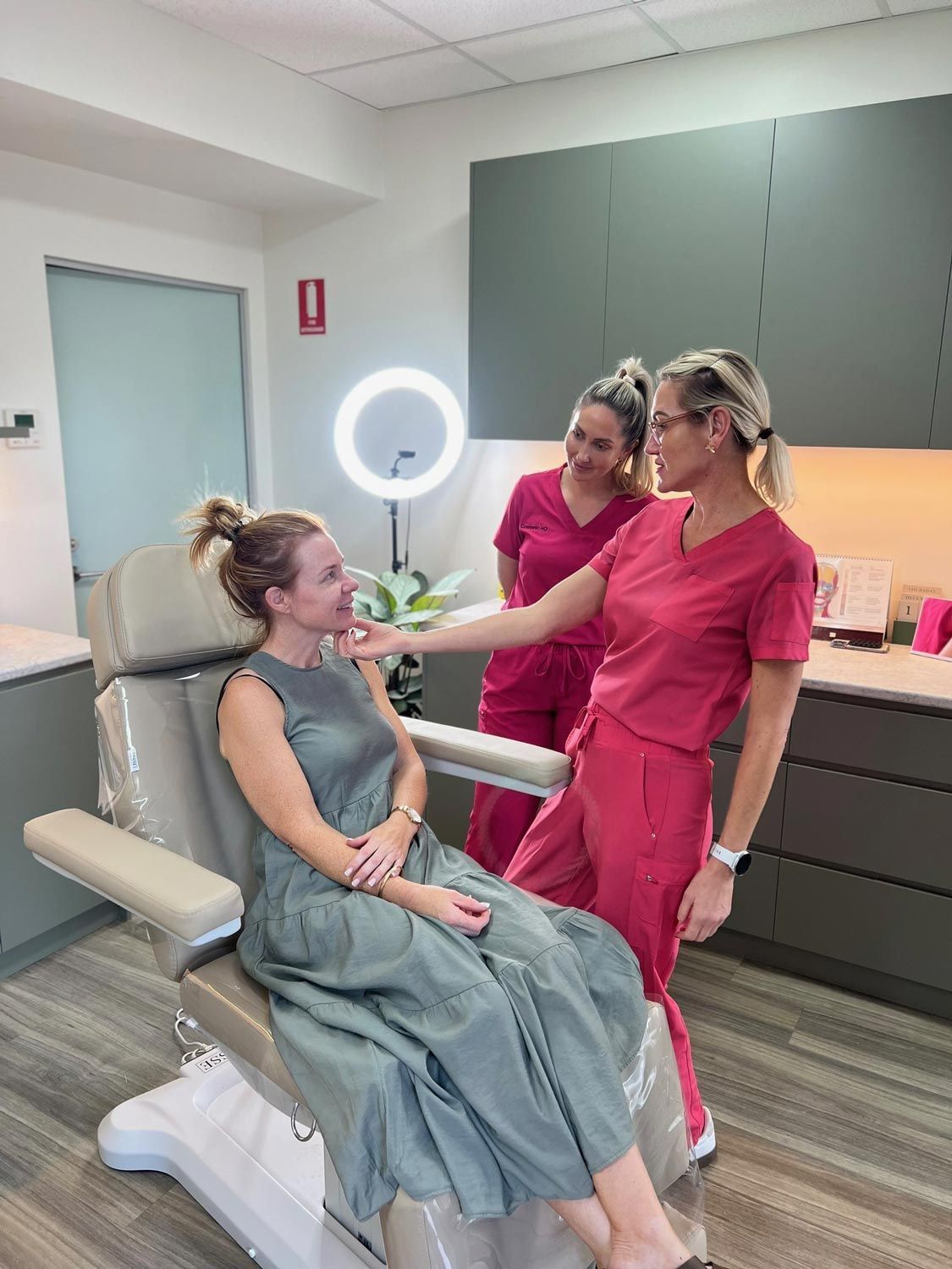 Woman in green dress consults with two medical professionals in pink scrubs, in a clinic.