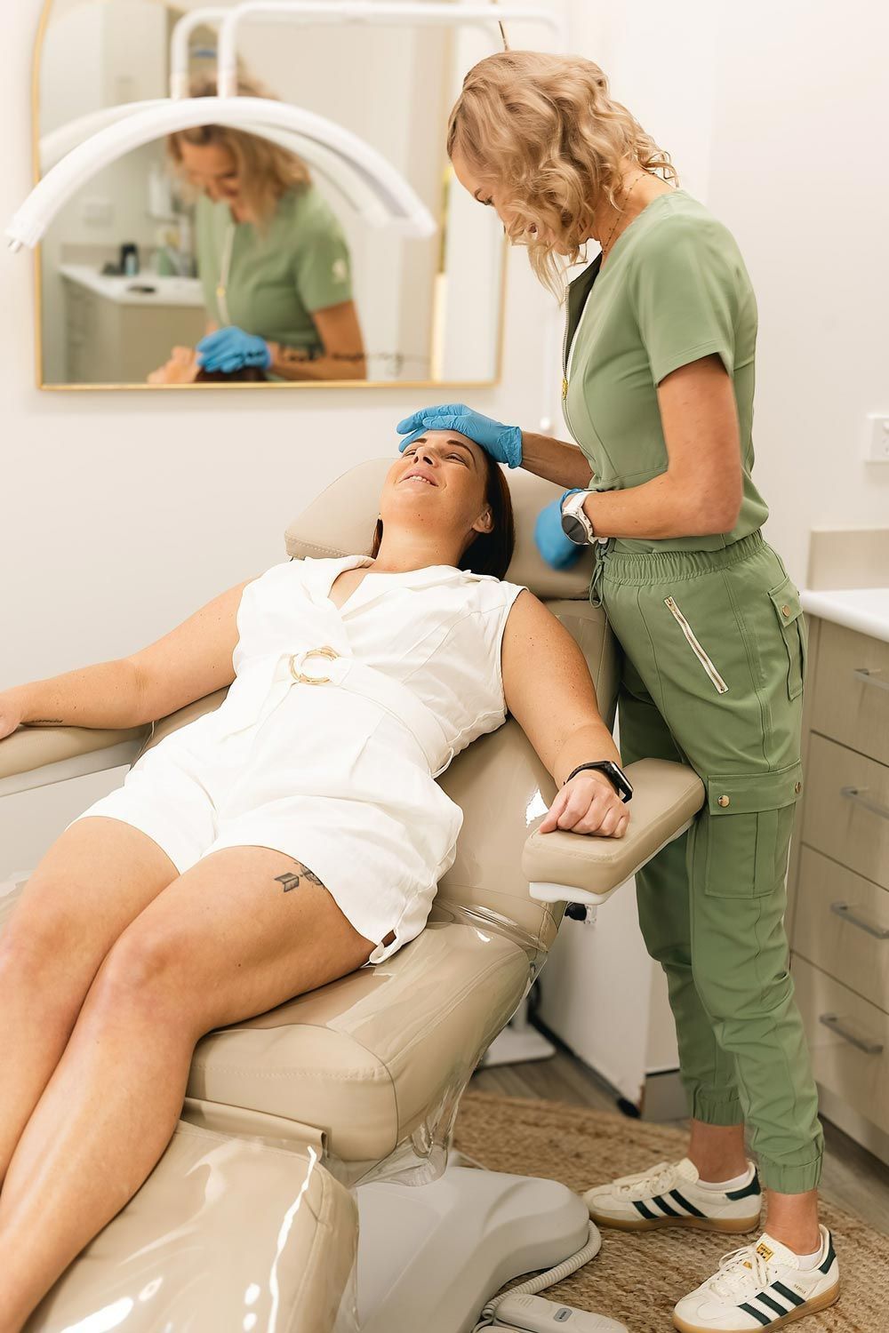 Woman in white gets a treatment, attended by a healthcare professional in green scrubs.