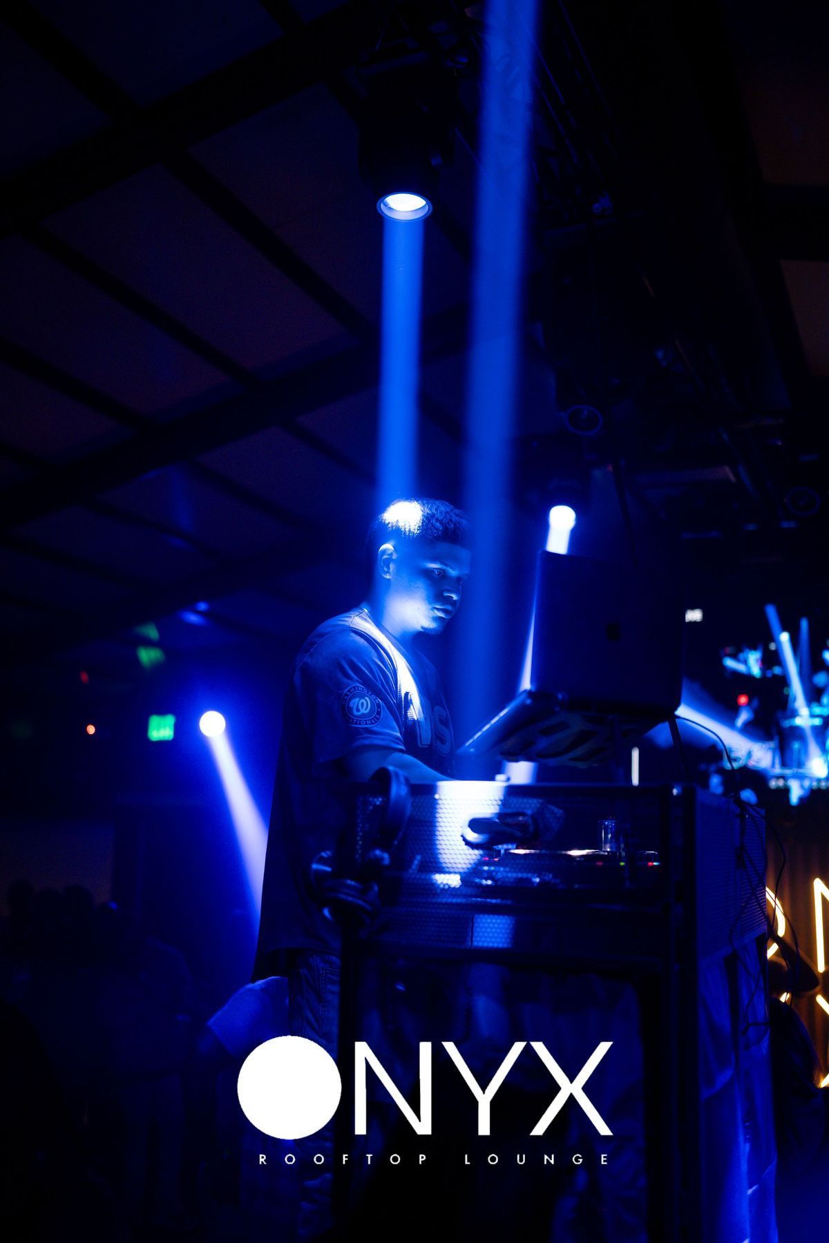 DJ at Onyx Club, performing. Blue stage lights, dark background, logo at bottom.