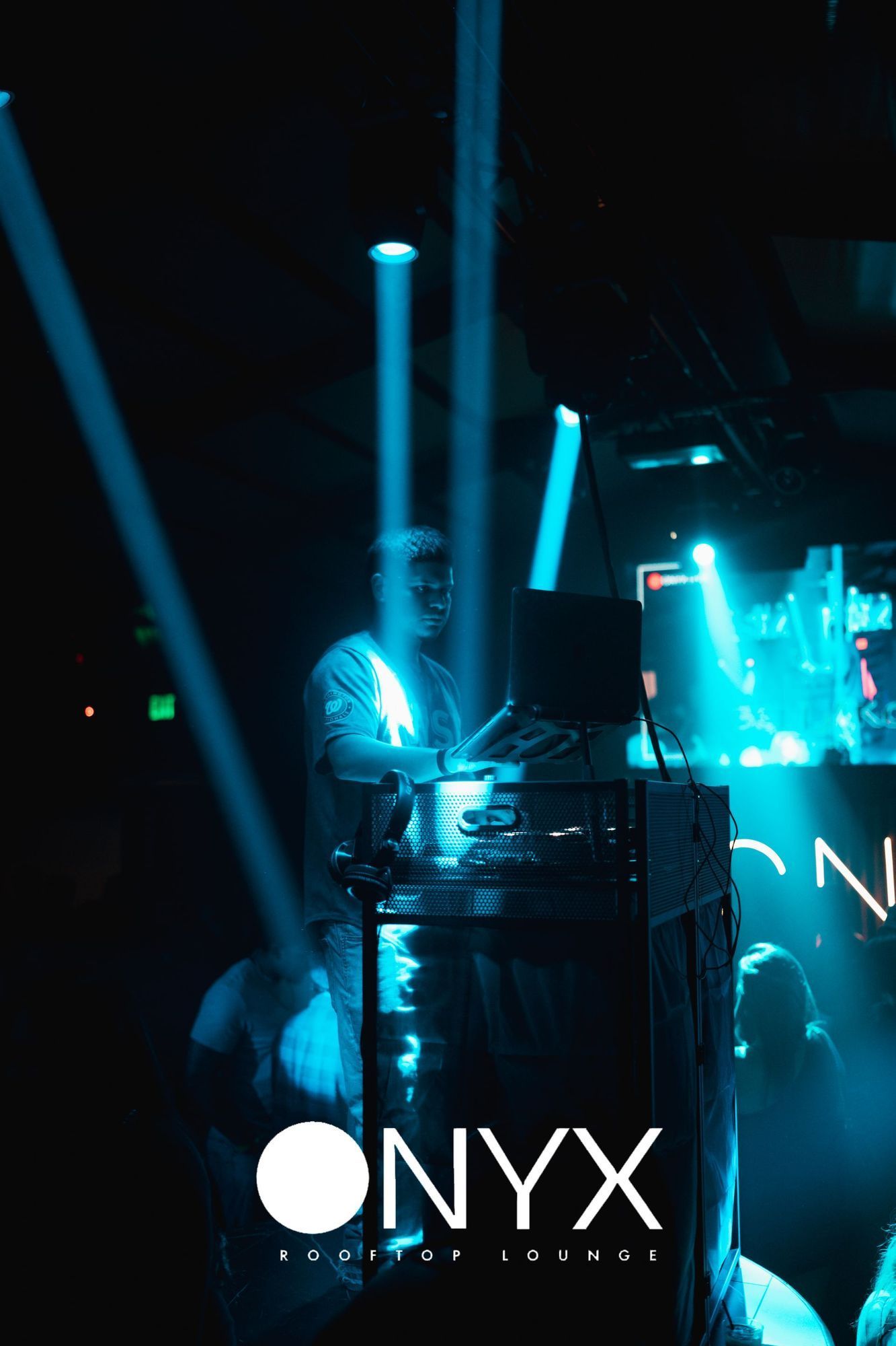 DJ performing at Onyx Rooftop in Illinois, bathed in blue lights, with equipment and a crowd visible.