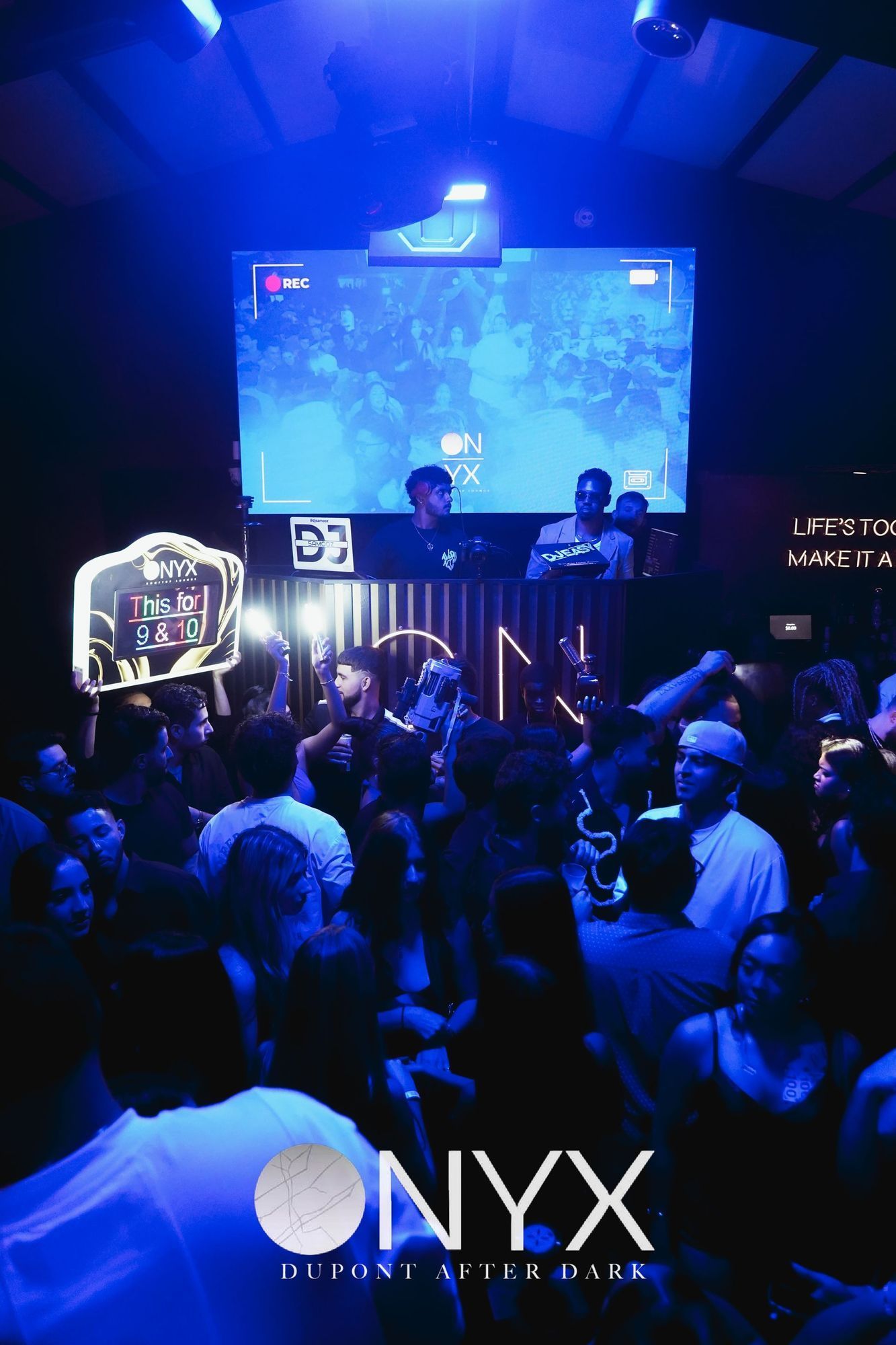 Nightclub scene: People dancing under blue lights, large screen, 