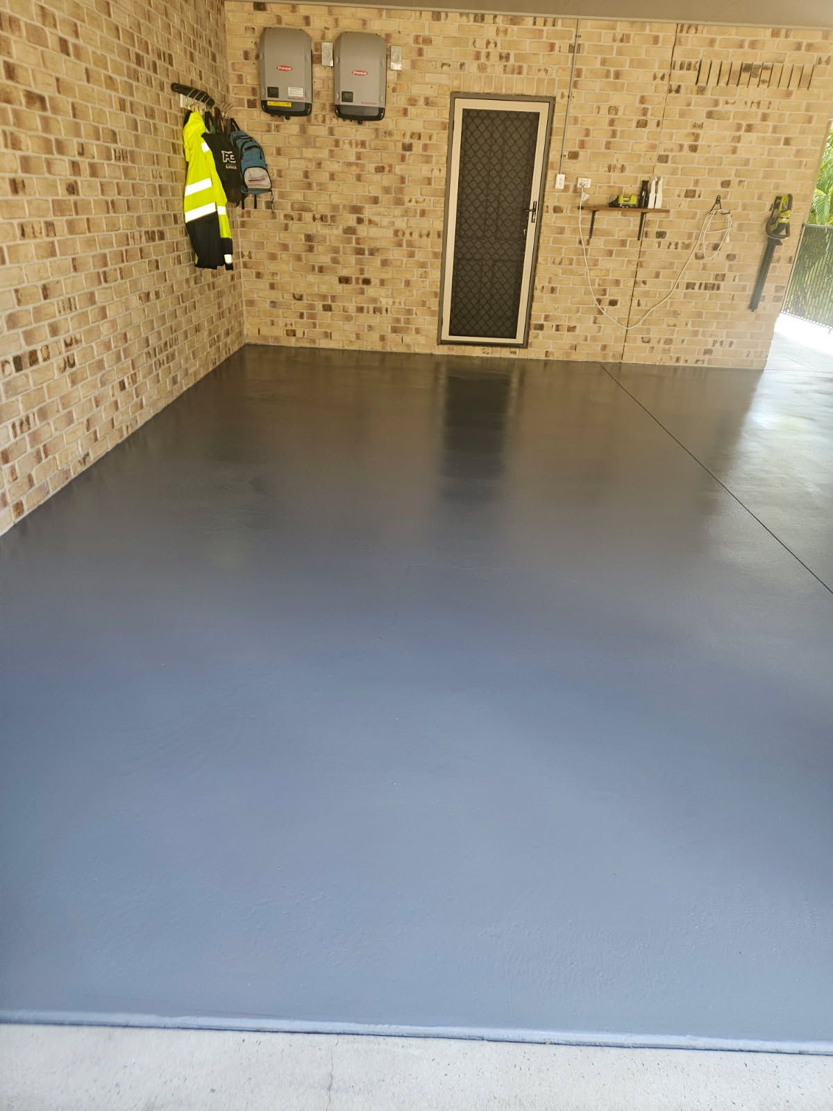 A Freshly Painted Smooth Gray Floor Inside a Carport With Brick Walls — Priority Painters in Gladstone Central, QLD
