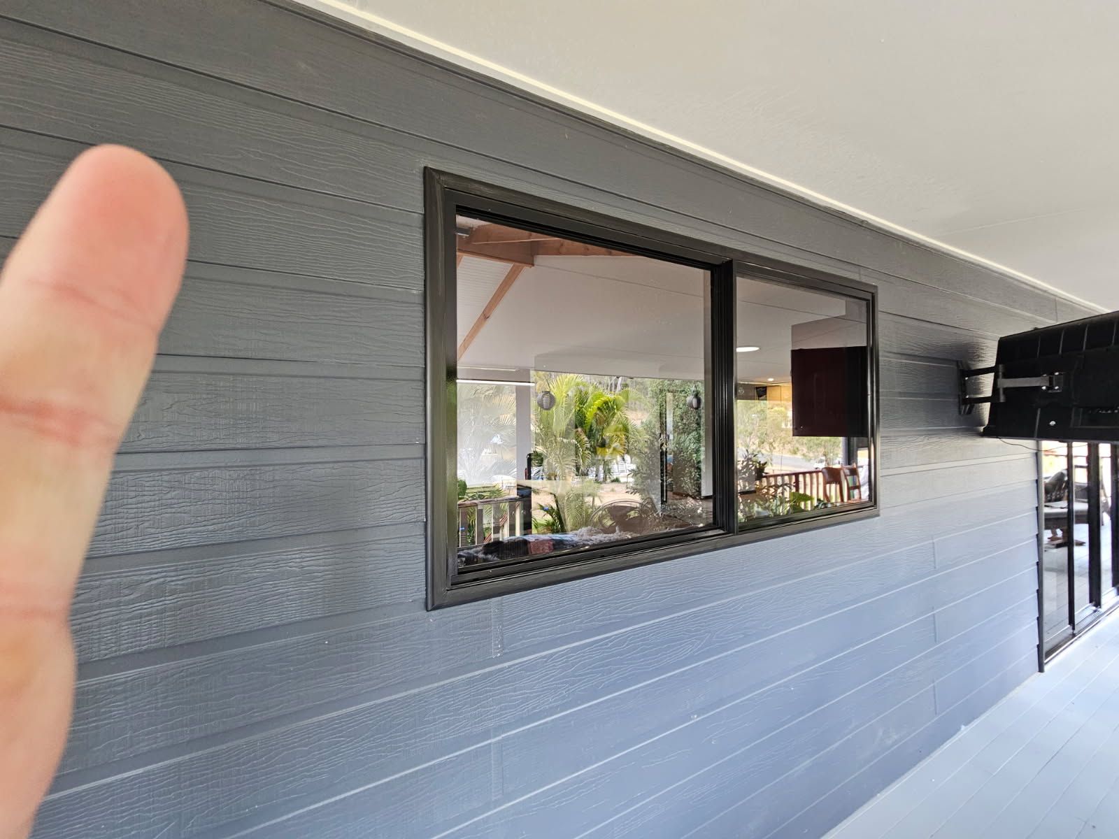 A Finger Points Toward Horizontal Grey Cladding on the Exterior Wall — Priority Painters in Gladstone Central, QLD