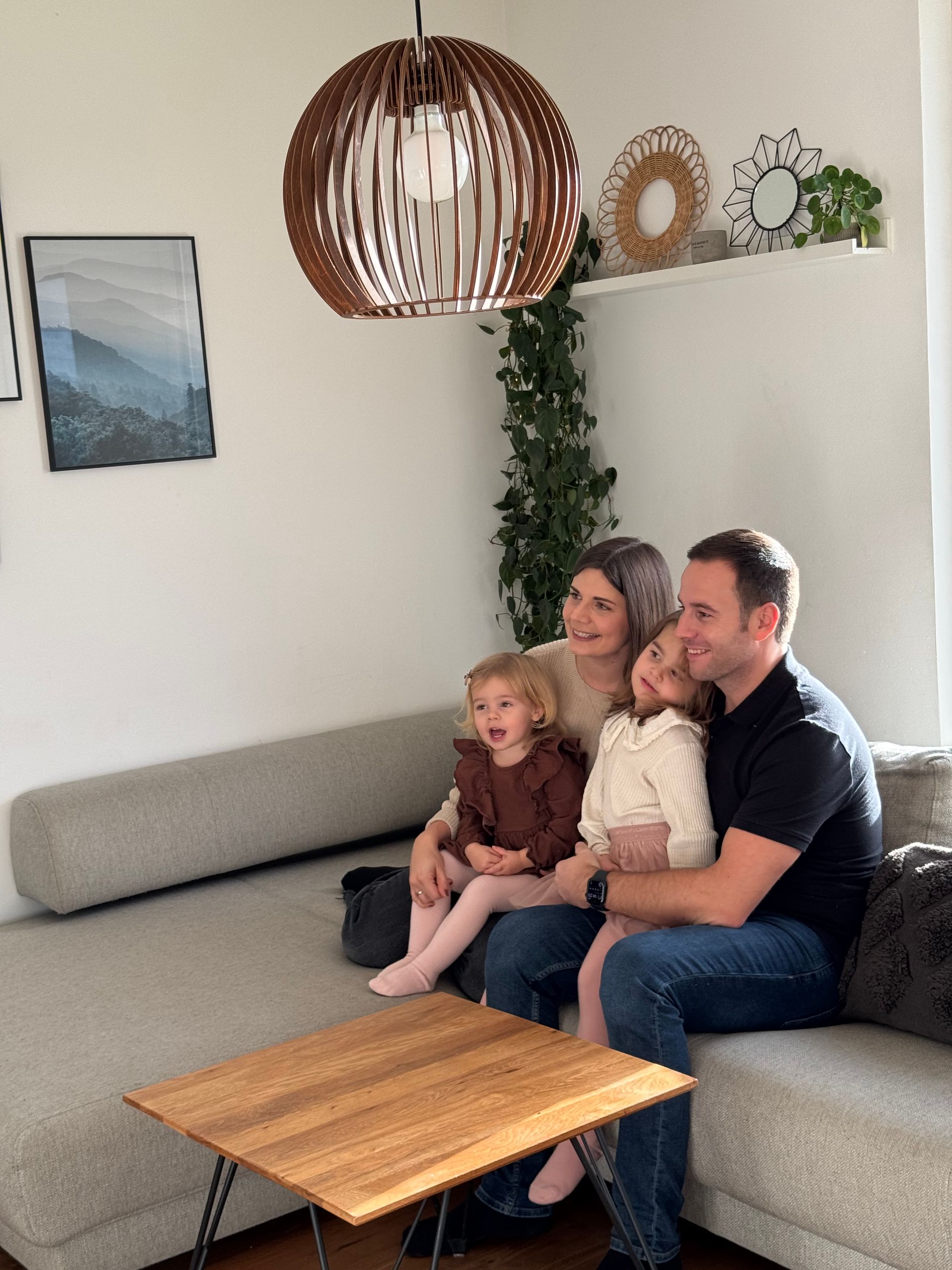 Lächelnde vierköpfige Familie, die auf einem grauen Sofa in einem hell erleuchteten Wohnzimmer posiert.