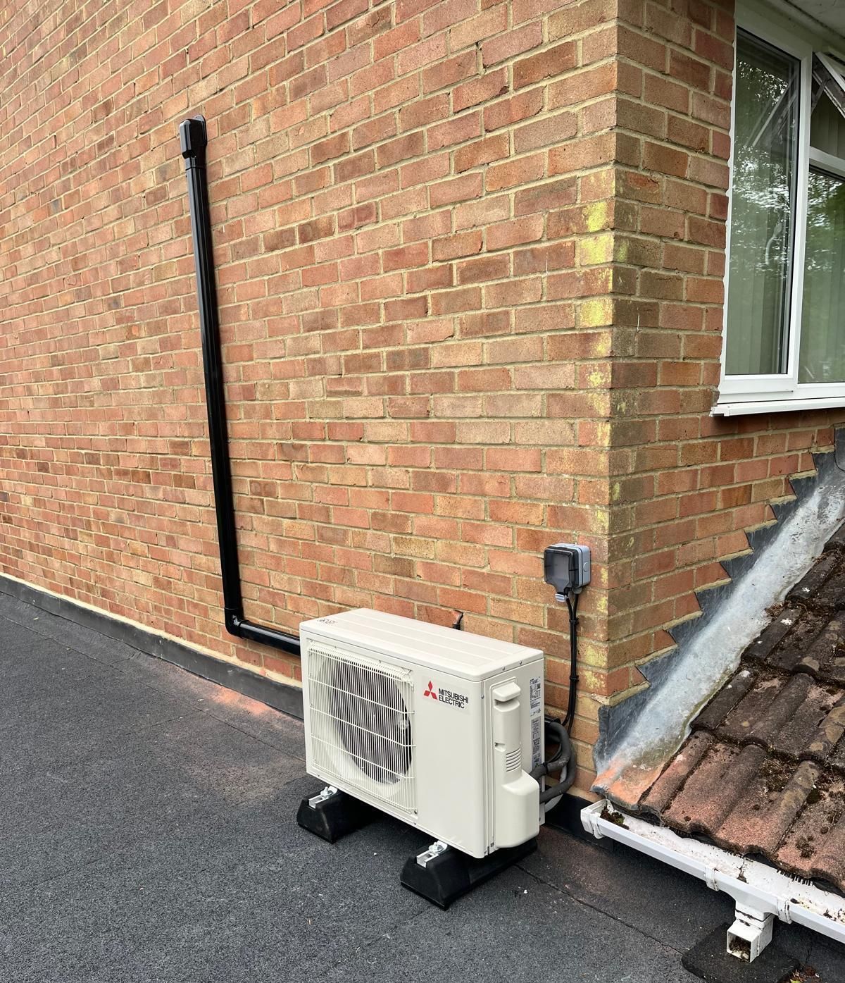 An air conditioning unit sits on black blocks next to a brick building.