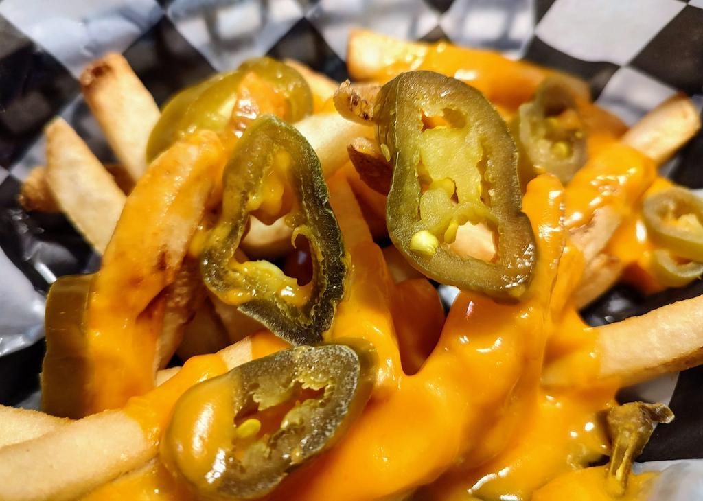 a close up of french fries with cheese and jalapenos