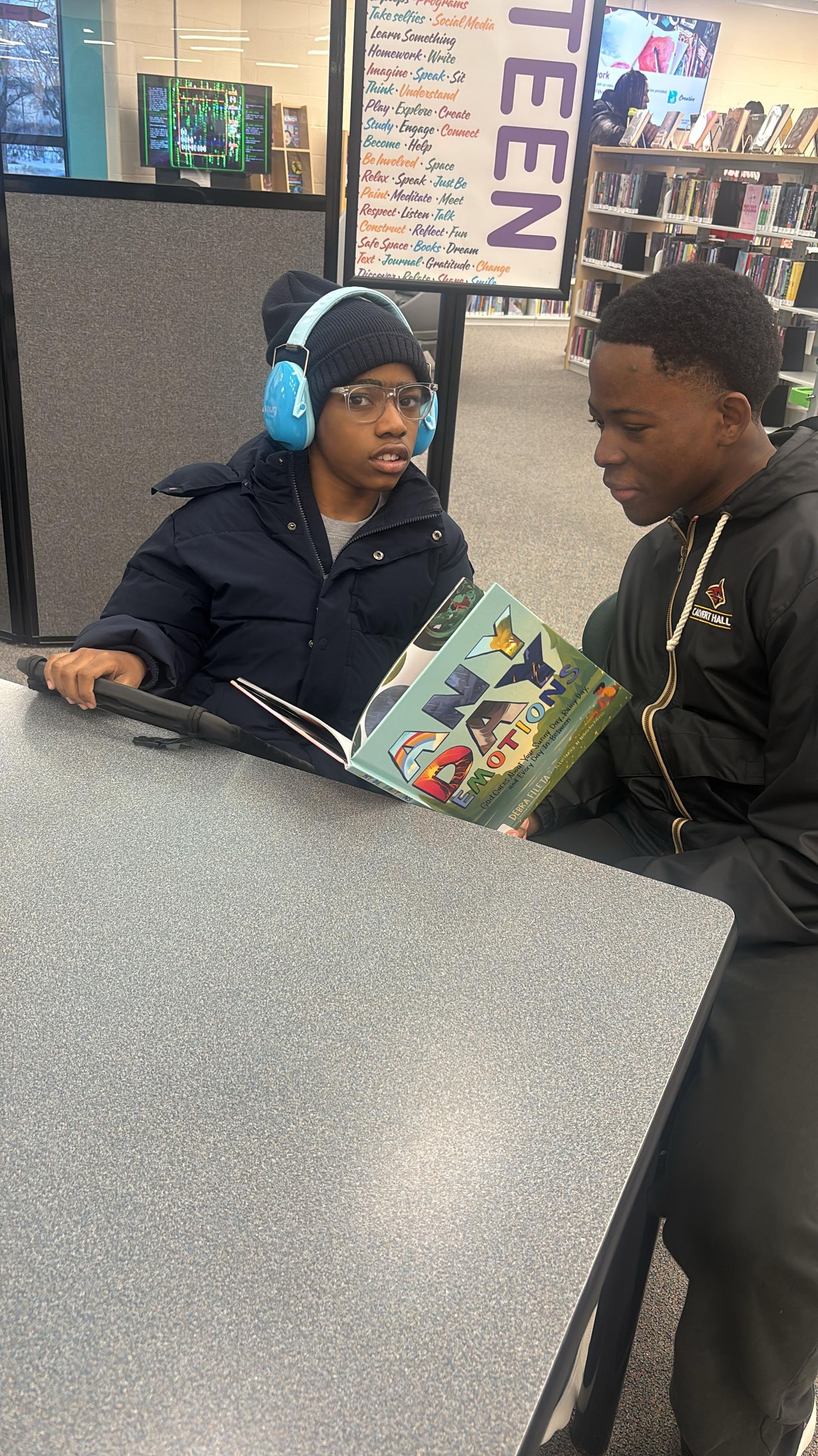 Two people reading a book at a table in a library. 