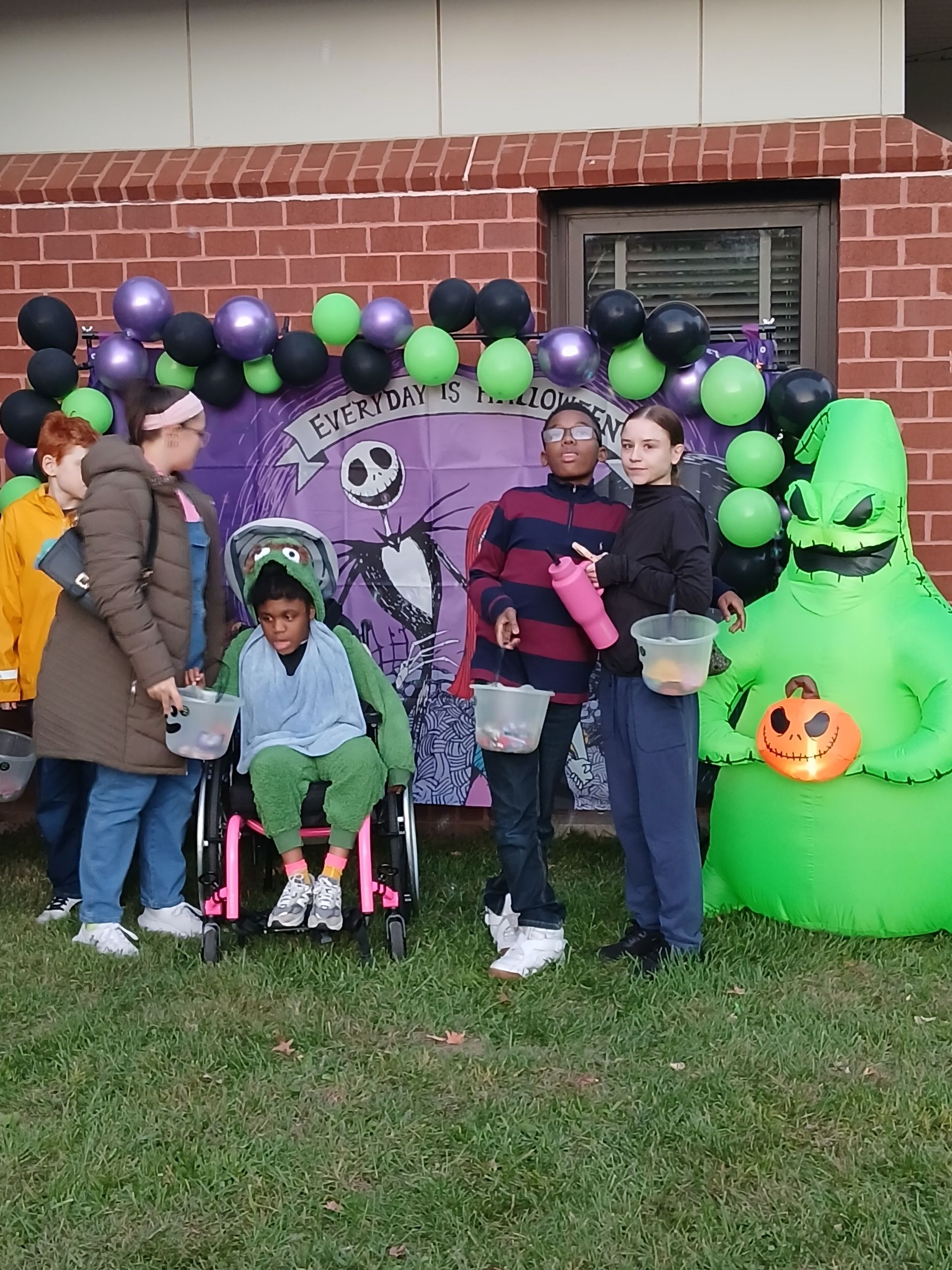 Group of people in Halloween costumes near decorations and a building.