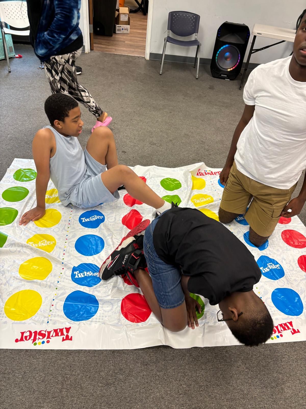 People playing Twister on a game mat with yellow, green, red and blue circles.