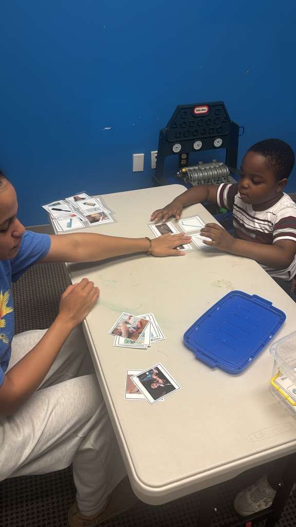 A person and a child seated at a table, sorting cards. Blue wall in the background.