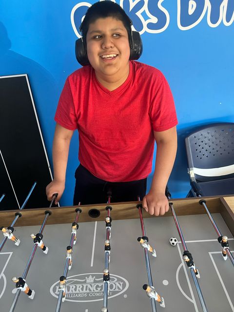 Boy in red shirt plays foosball, smiling.