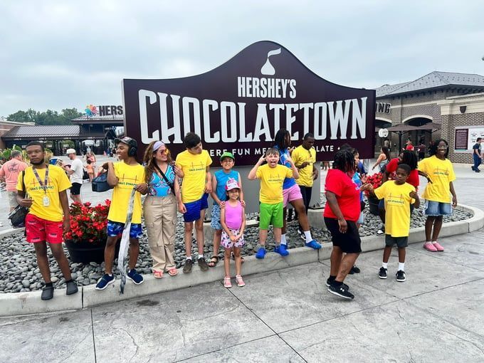 Group of people in yellow shirts pose in front of a Hershey's CHOCOLATE TOWN sign.