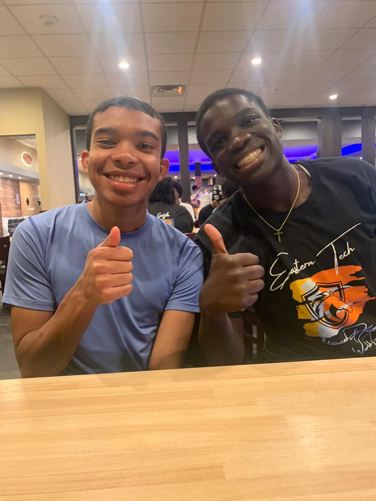 Two young men smiling and giving thumbs up at a restaurant. 