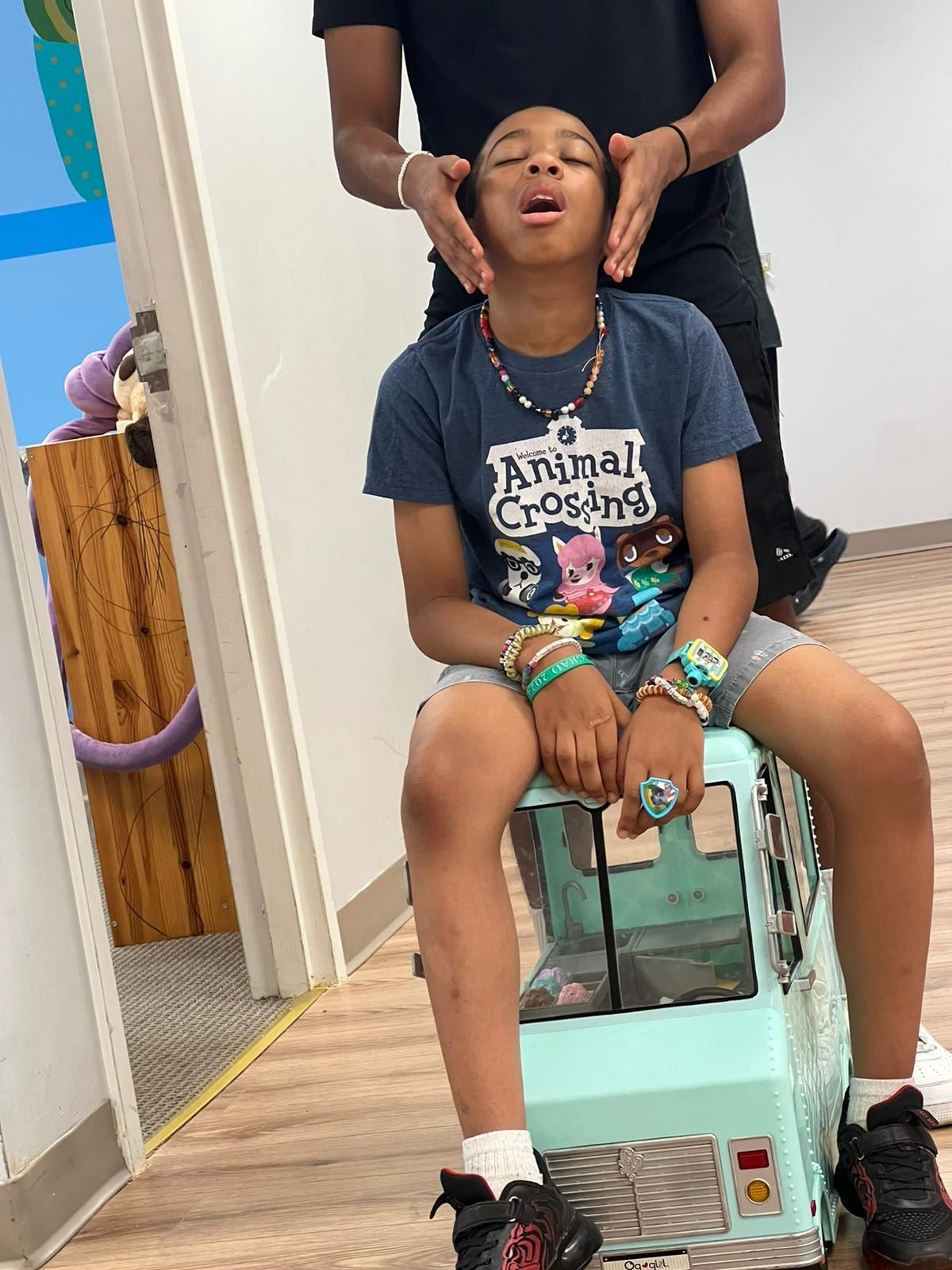 Child on a toy vehicle, with hands on their face, an adult's hands are on either side of their head.