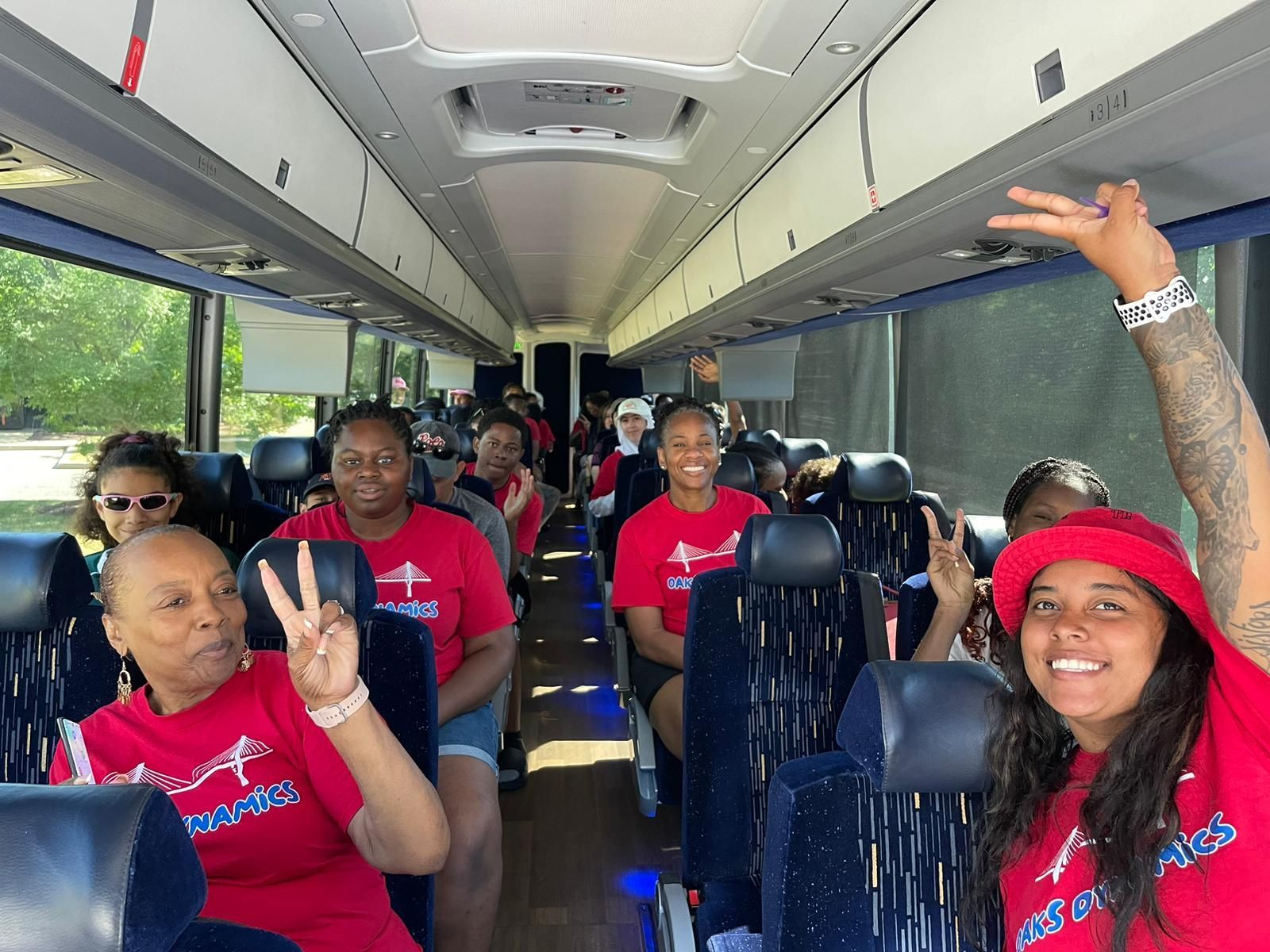People on a bus, wearing red shirts. Woman in red hat waves, smiles. 