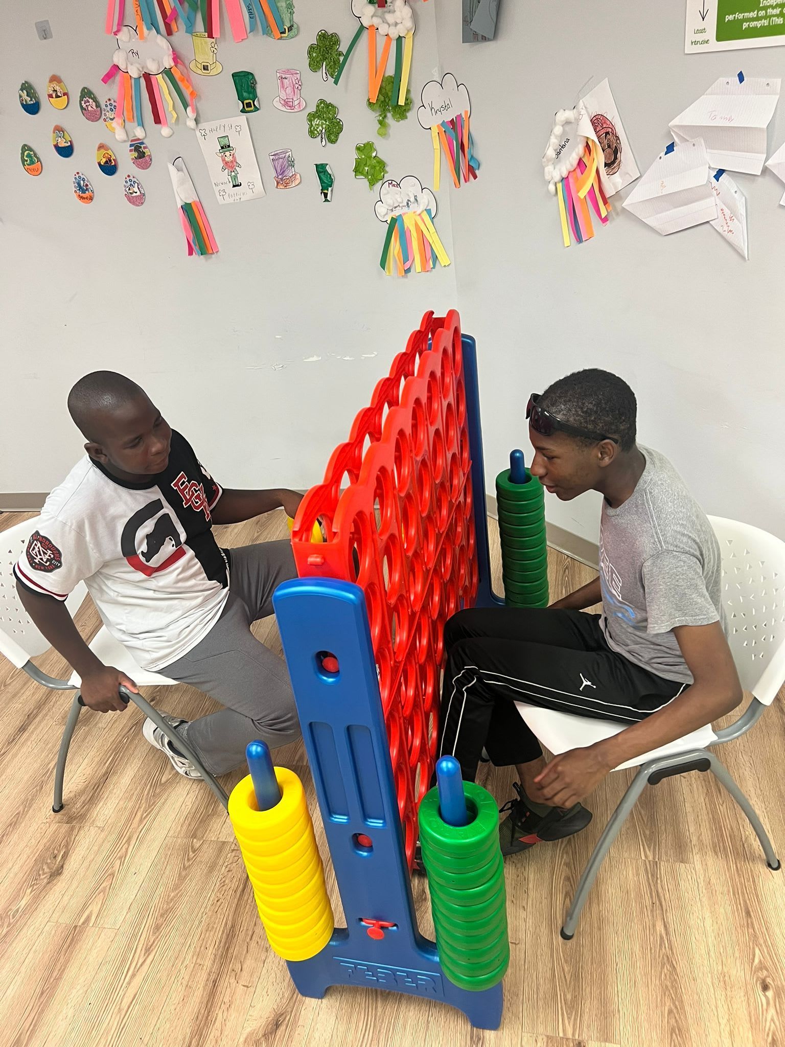 Two people playing a giant Connect Four game in a room with artwork on the wall.