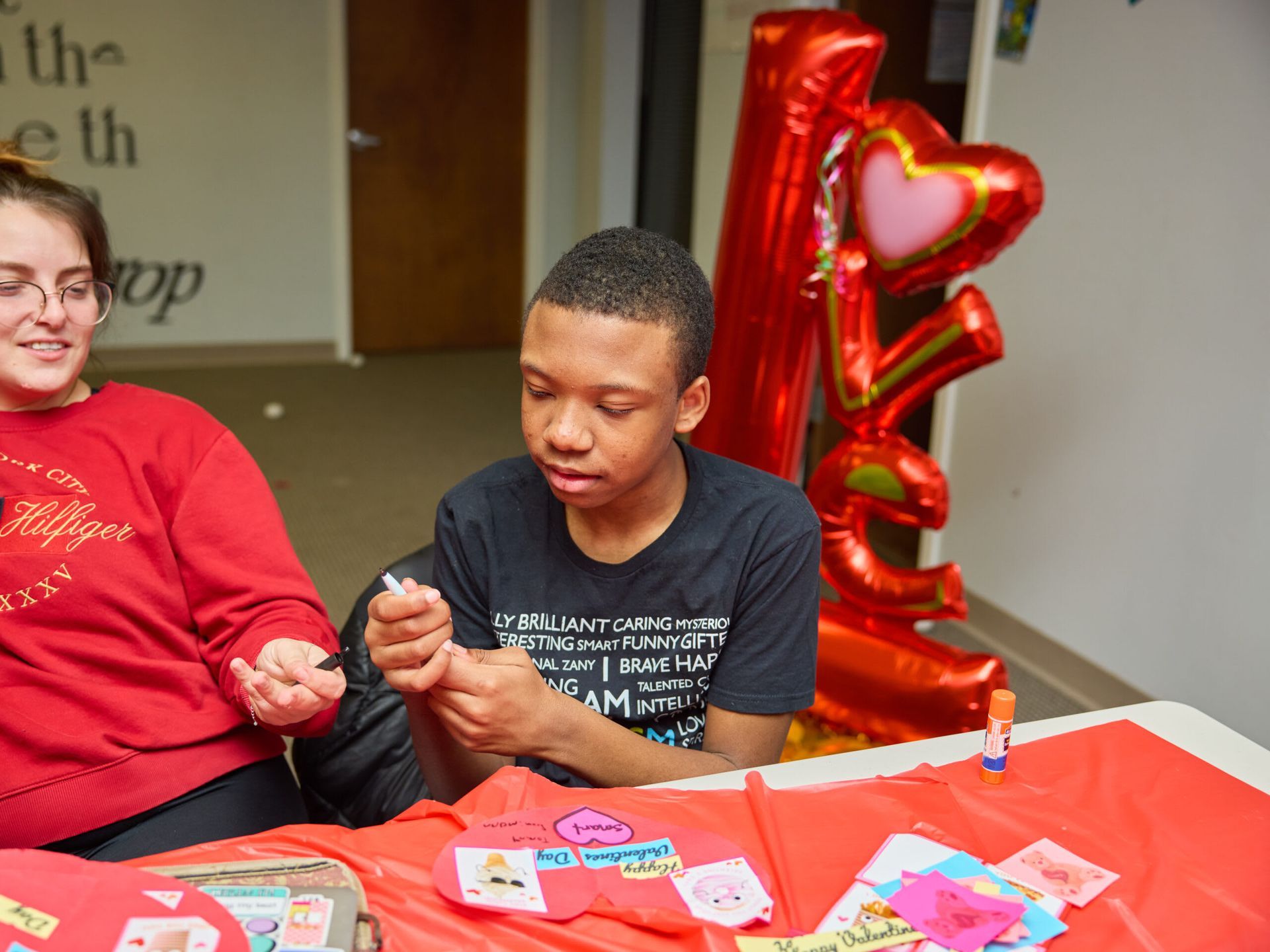 Teen making Valentine's crafts at a table with a red tablecloth.