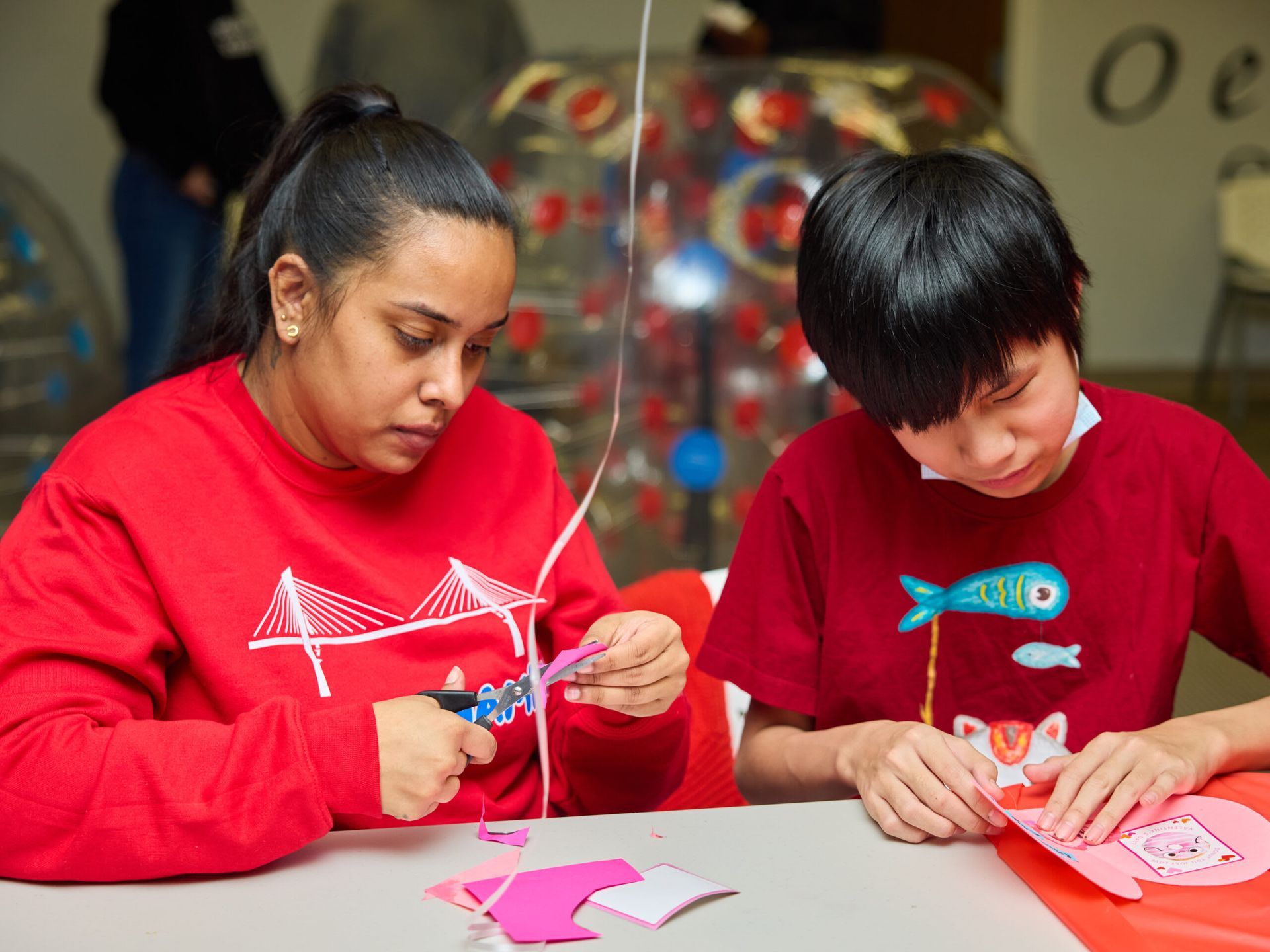 Woman and person crafting together, using scissors and paper at a table. 