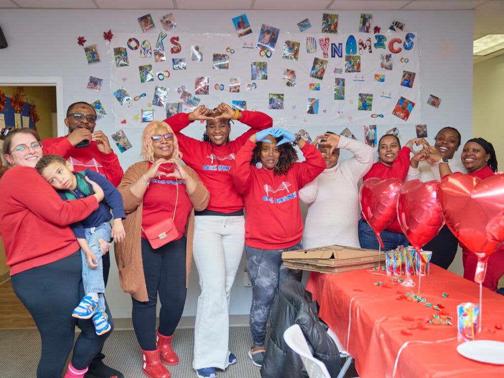 Group of people in red shirts making heart shapes with their hands. 