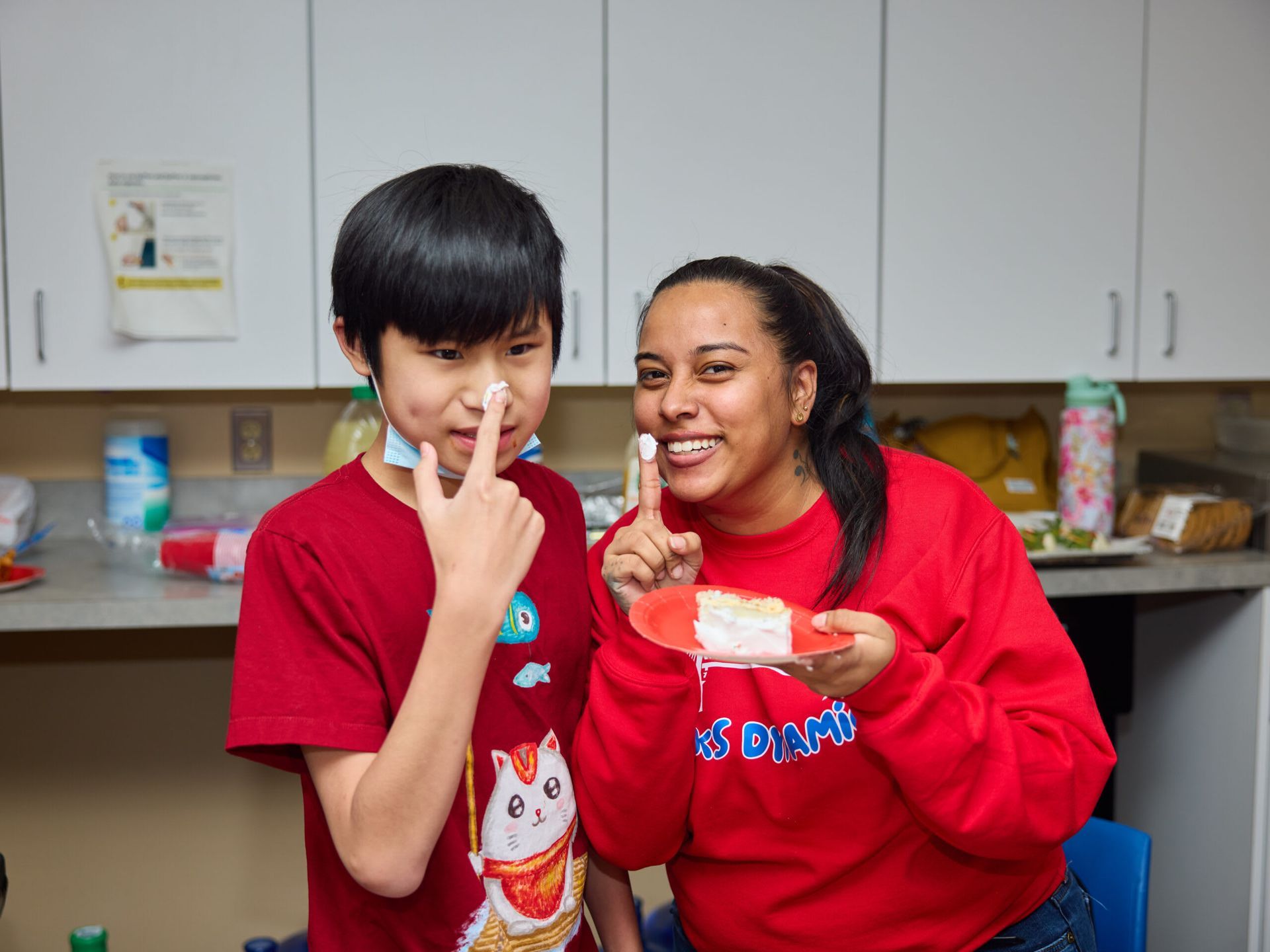 Boy and woman with cream on their noses, smiling. Indoors, kitchen.