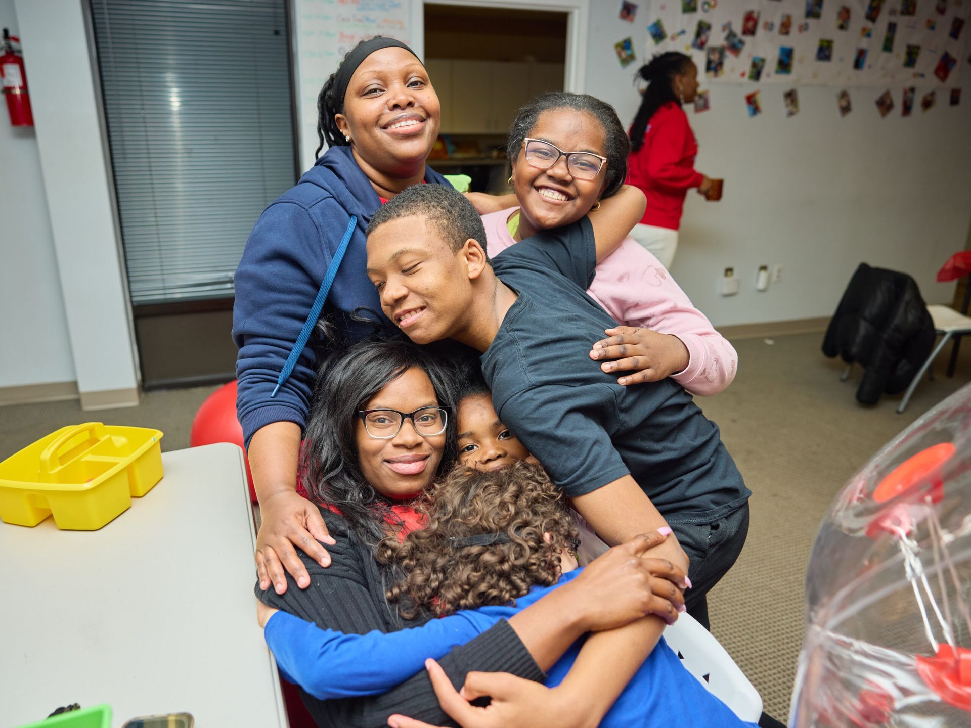 Five people in a close group hug, smiling.  