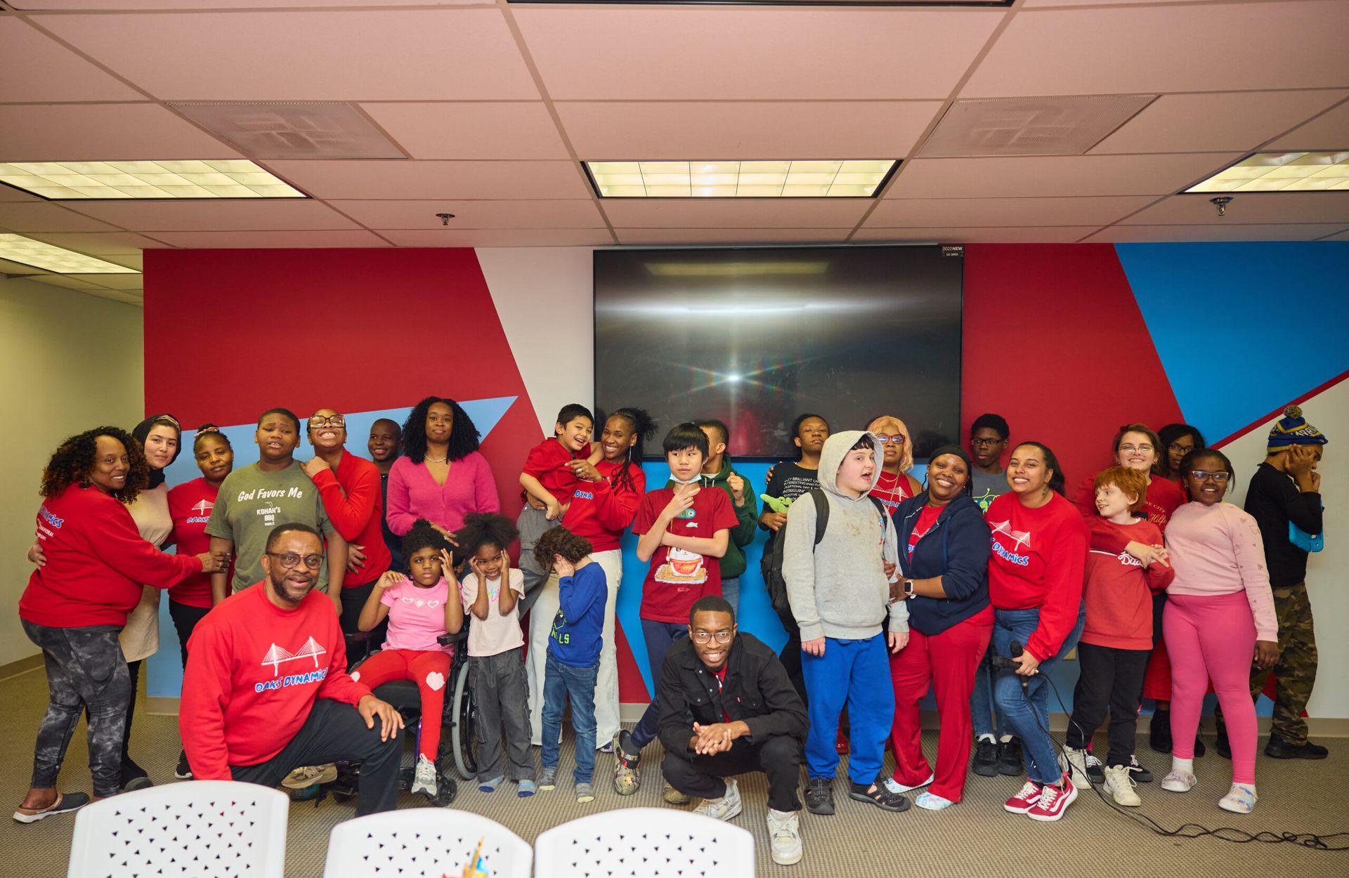 Group of people in red shirts and outfits pose in a room with red and blue accents.