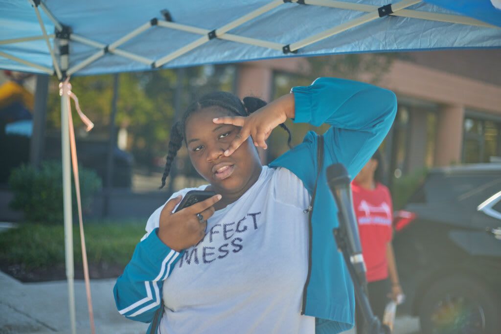 Person making peace signs with teal jacket and shirt that says 