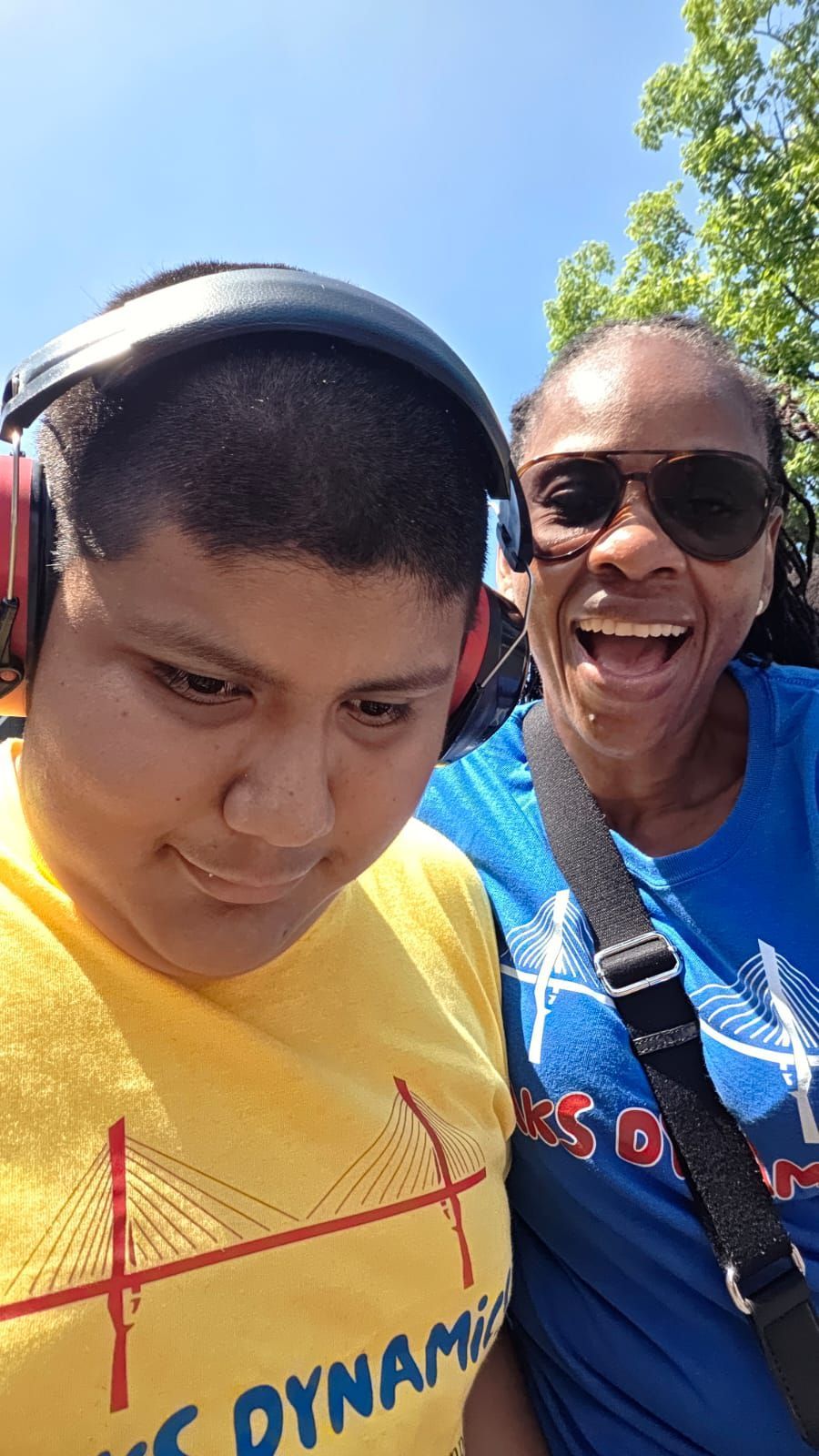 Two people outdoors: one wearing headphones, the other smiling. 