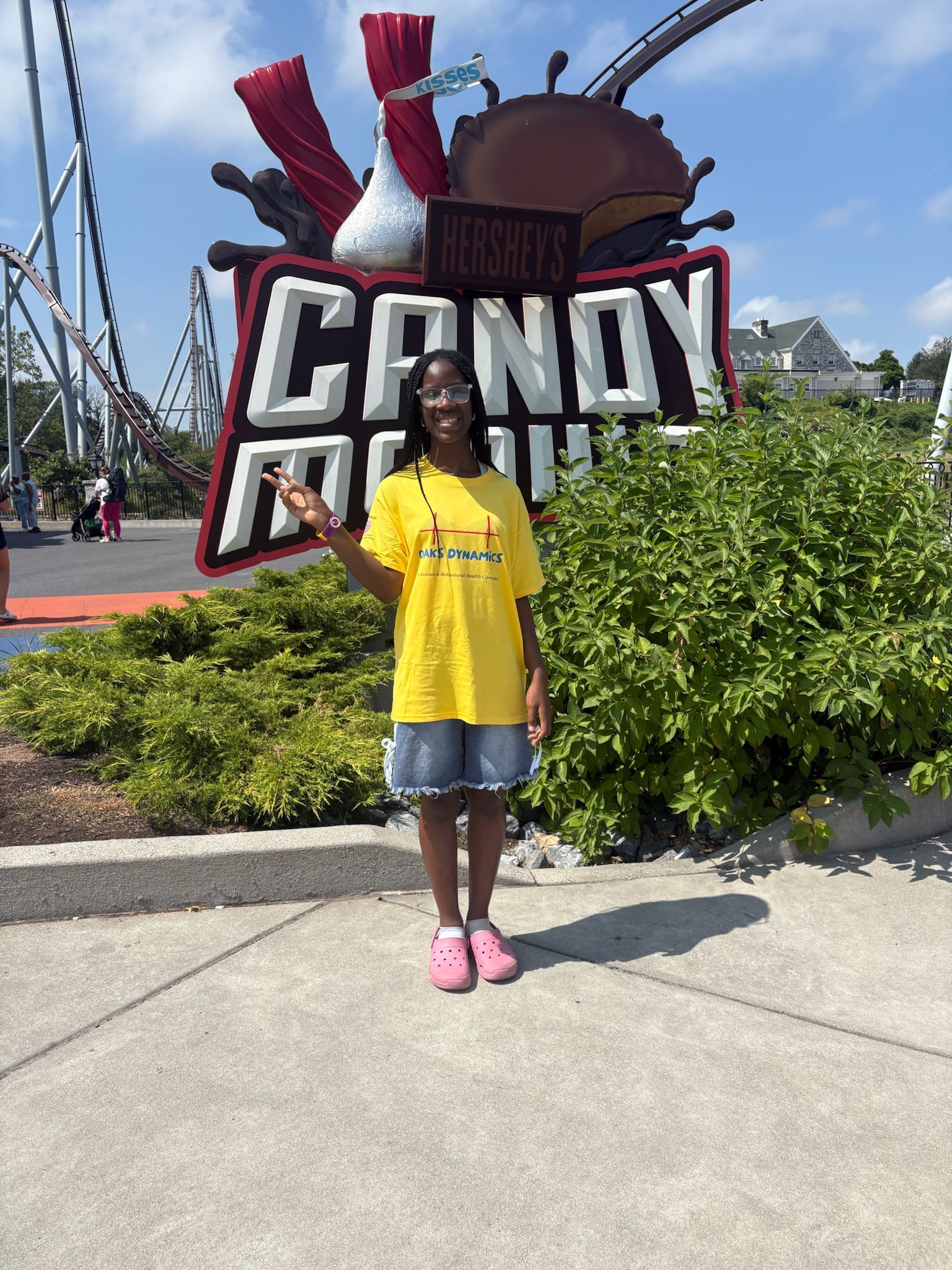 Person in yellow shirt and denim shorts points at the Hershey's Candy Mania sign at Hersheypark.
