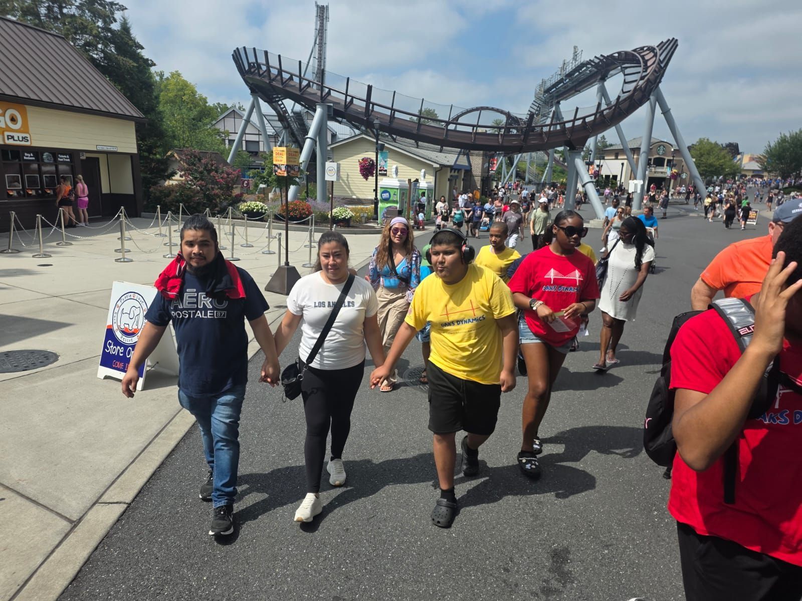 People walking on a paved pathway, roller coaster in background.