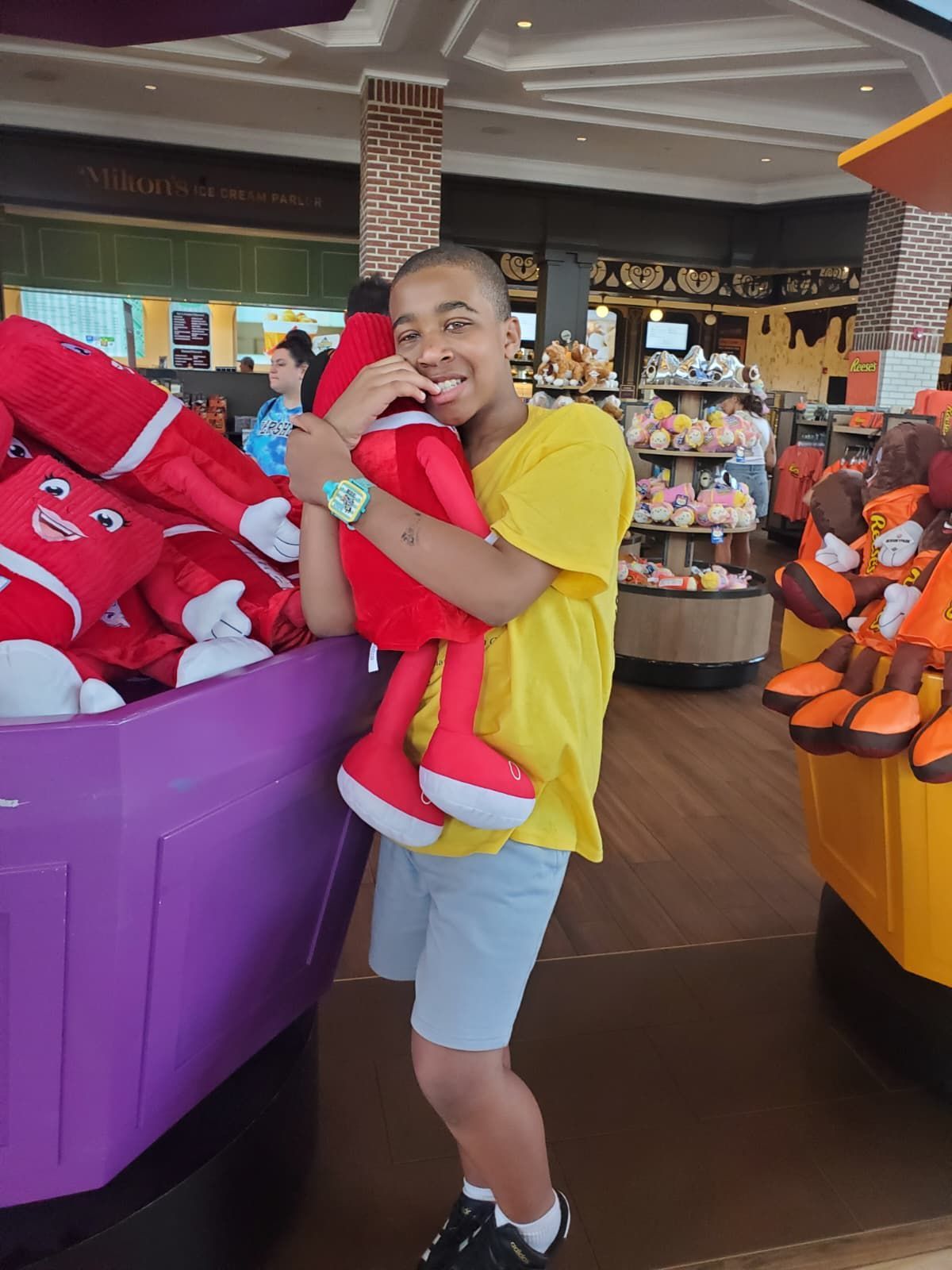 Person smiles, hugging a large red plush toy in a shop. 