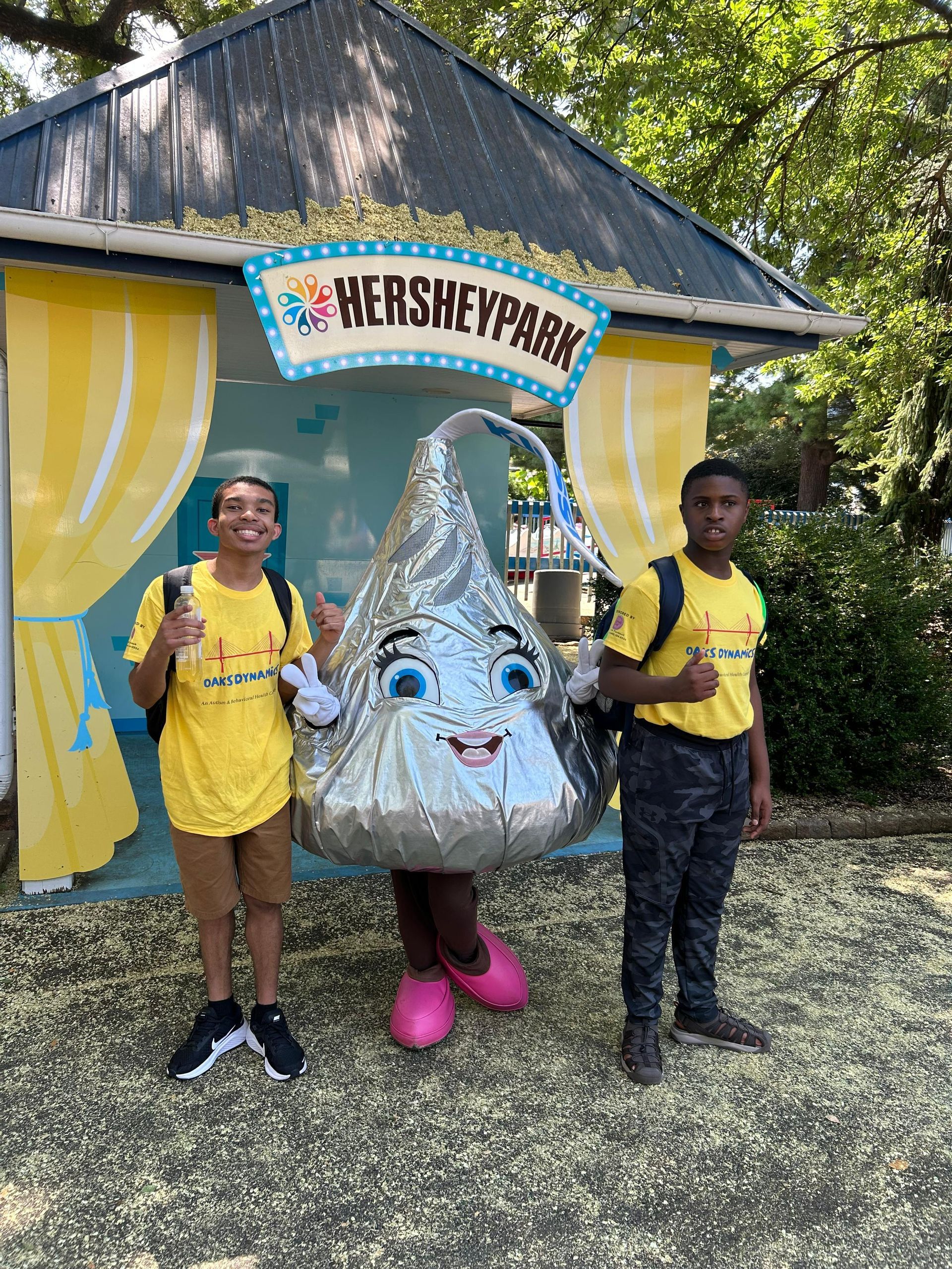 Two people and Hershey Kiss mascot pose in front of HersheyPark entrance.