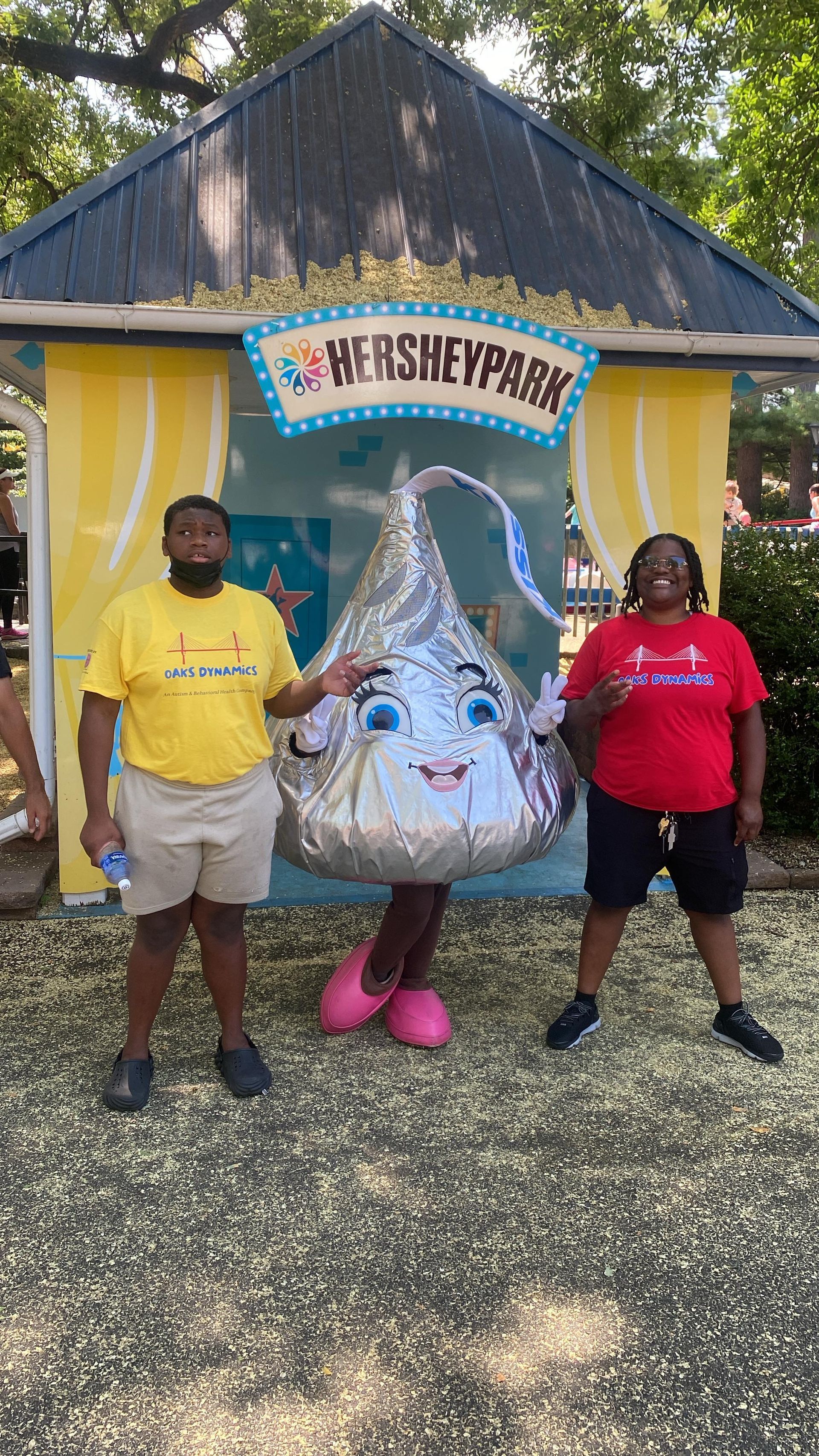 Two people pose with Hershey Kiss mascot at HersheyPark entrance.