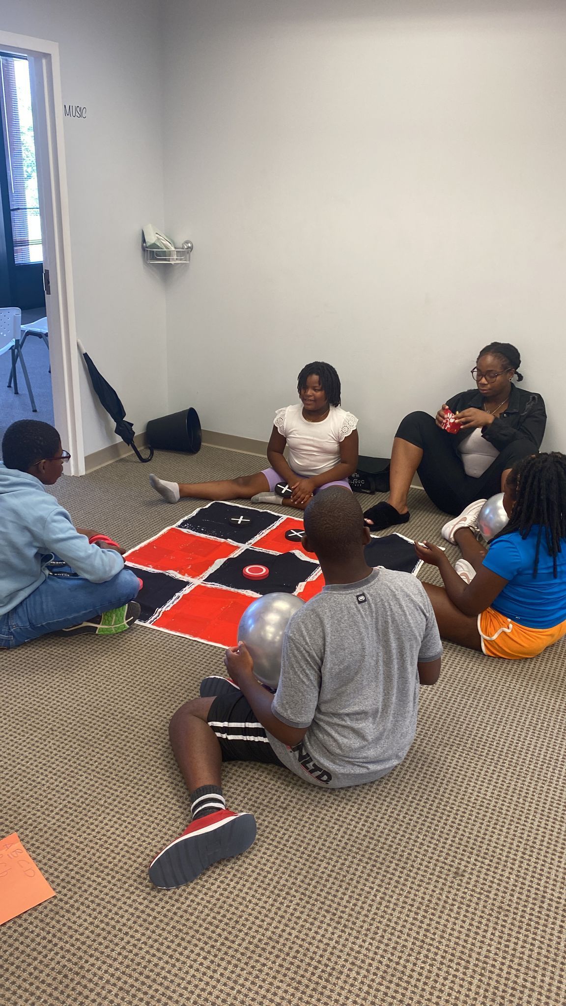 Two children play in a small inflatable pool filled with toys inside a room.